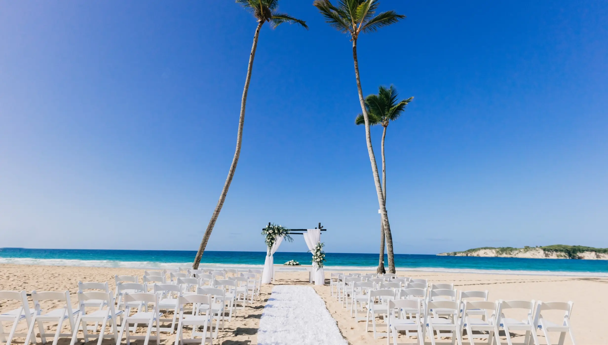 Beachfront wedding ceremony with white chairs and floral arch at Dreams Macao Beach, Punta Cana