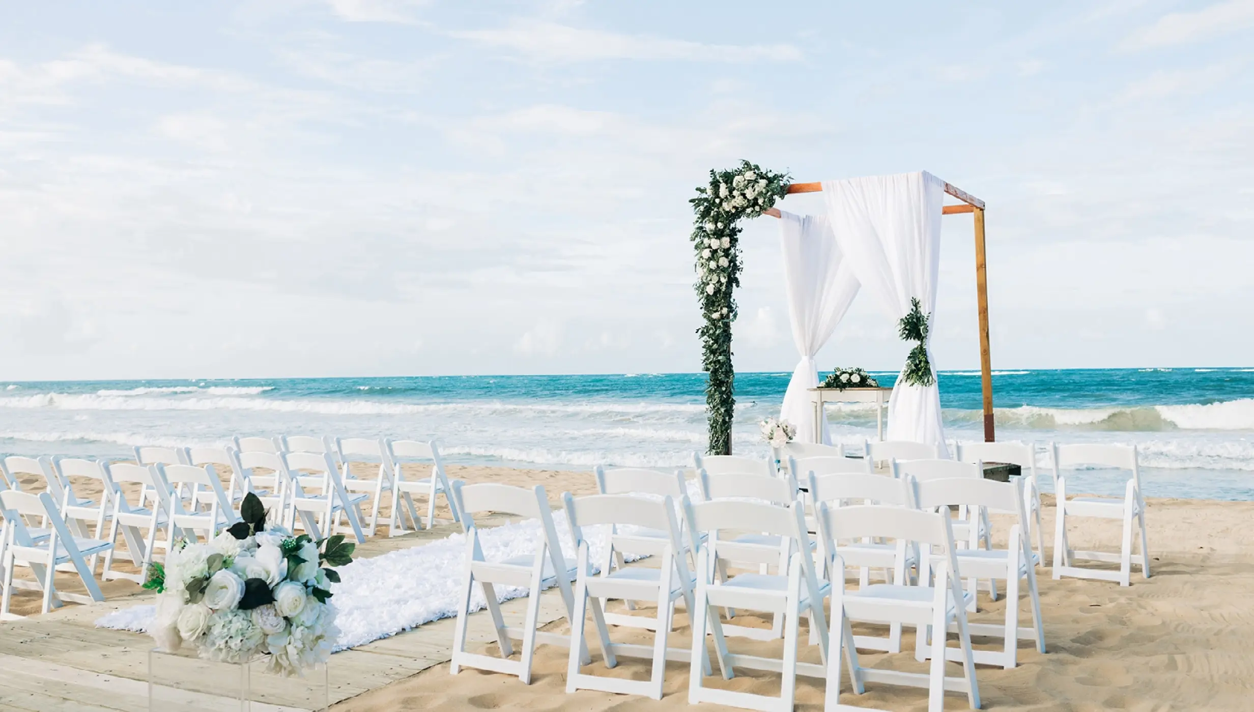 Beach wedding ceremony with white chairs and floral arch at Dreams Macao Beach, Punta Cana