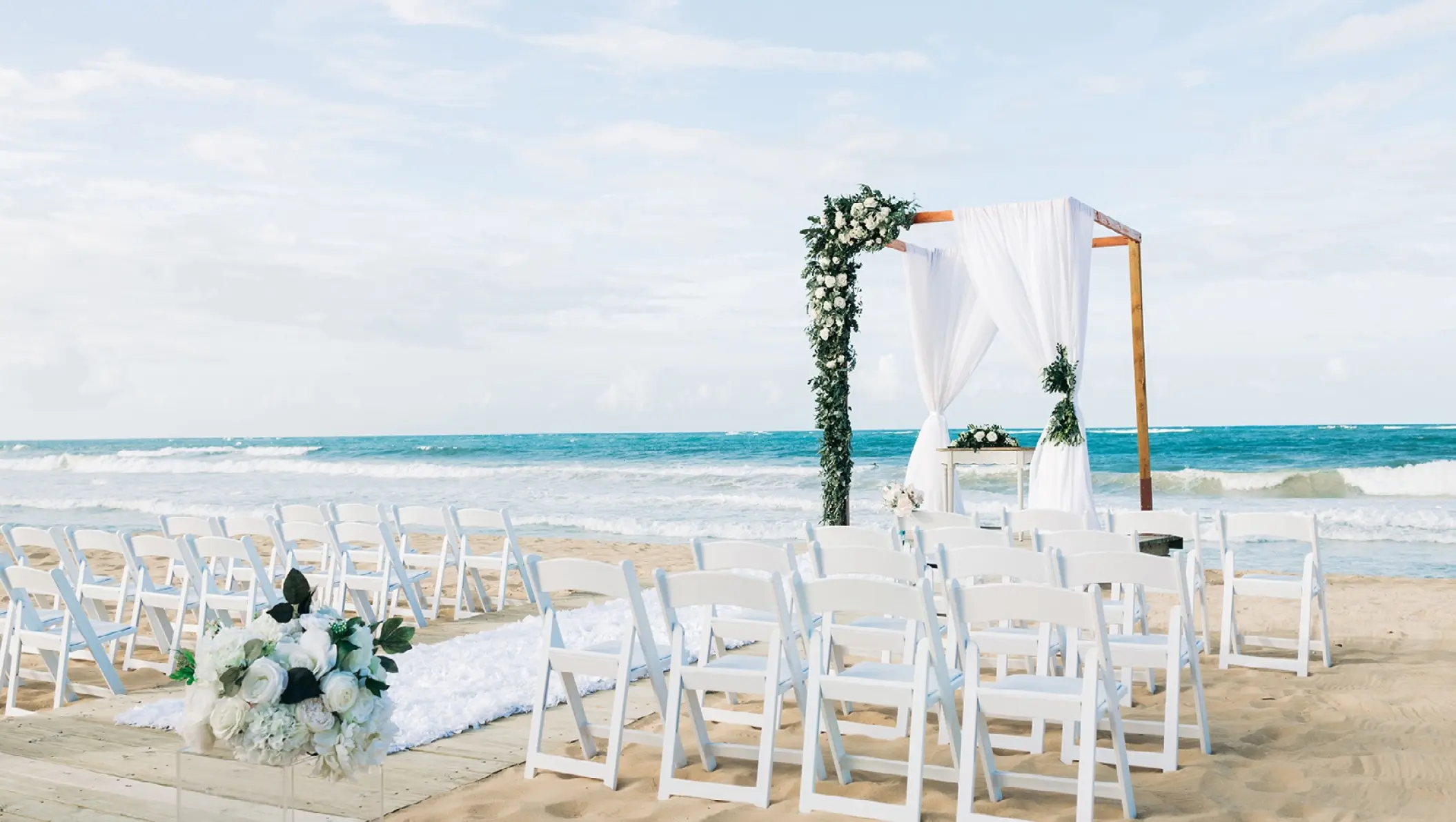 Beach wedding ceremony with white chairs and floral arch at Dreams Macao Beach, Punta Cana