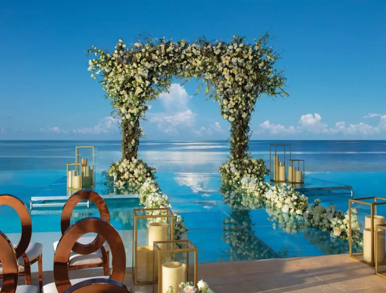 Waterfront wedding ceremony with floral arch and glass aisle over the pool at Dreams Natura, Riviera Maya
