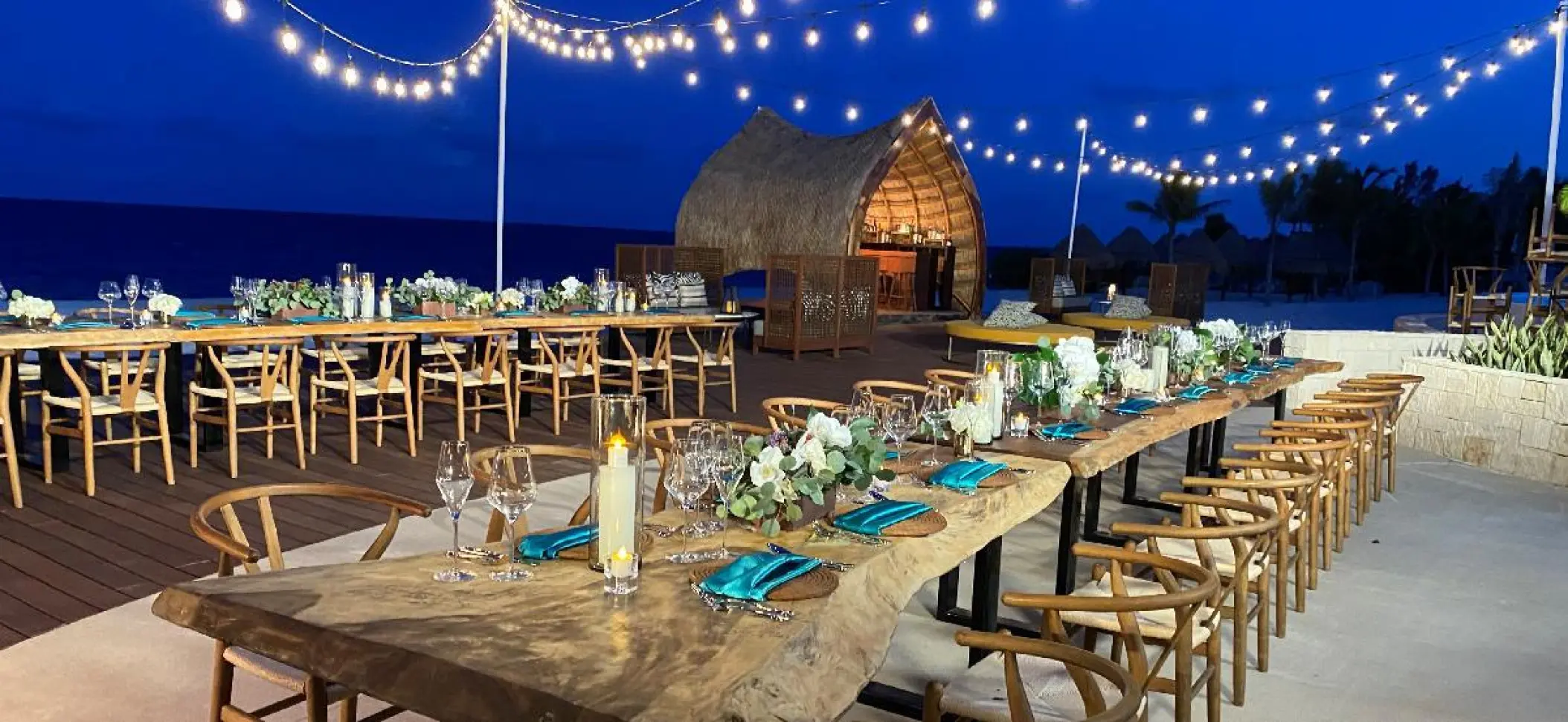 Evening wedding reception on a wooden deck with string lights at Dreams Natura, Riviera Maya