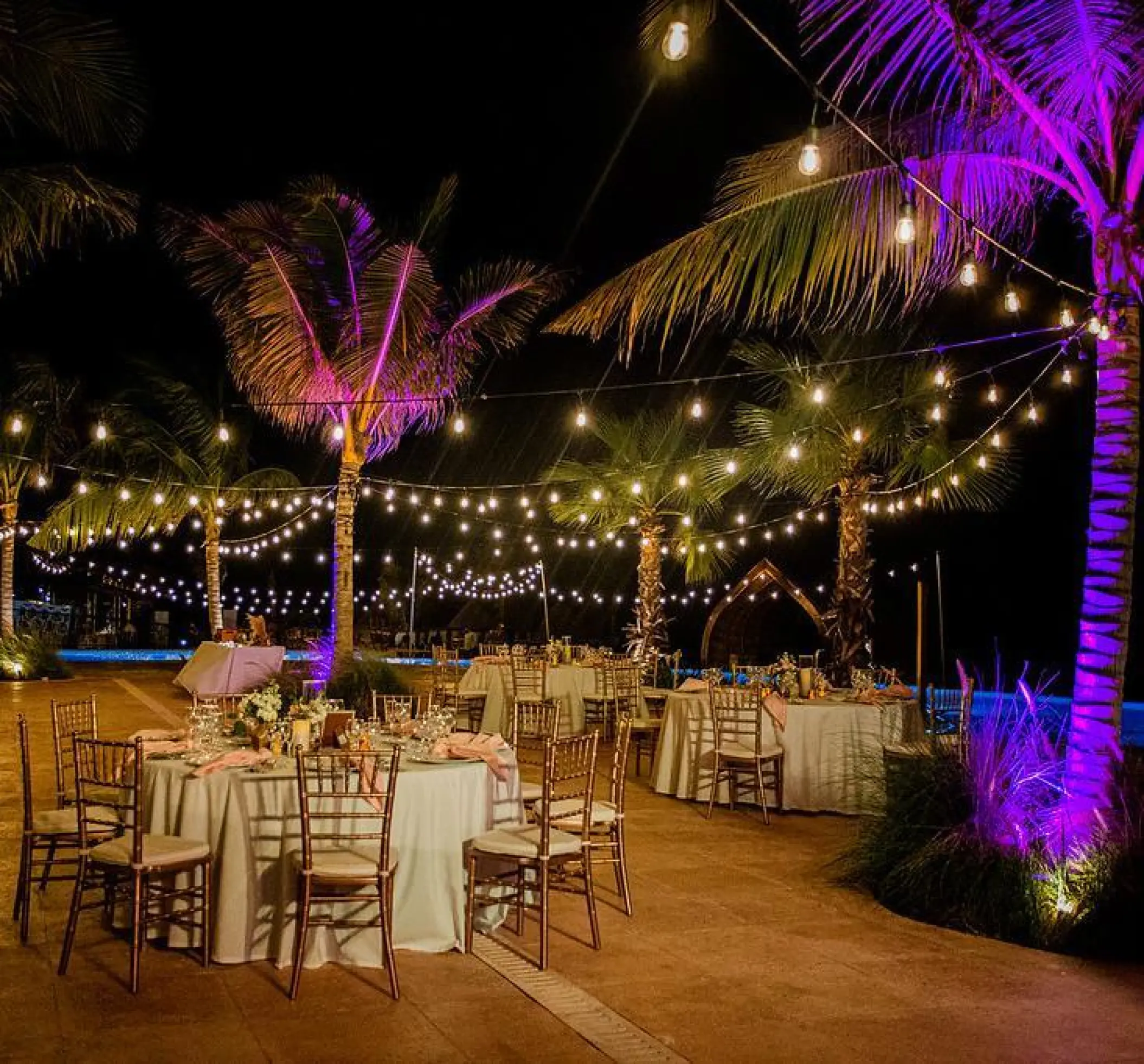 Pool terrace wedding reception with string lights and purple palm tree lighting at Dreams Natura, Riviera Maya