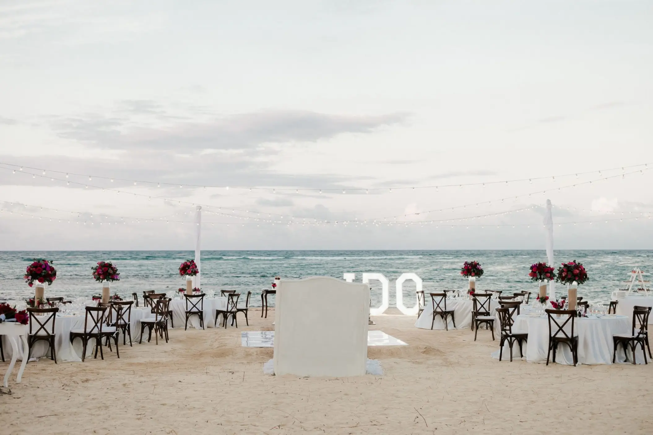Beachfront wedding reception setup with string lights and white tables at Dreams Onyx, Punta Cana