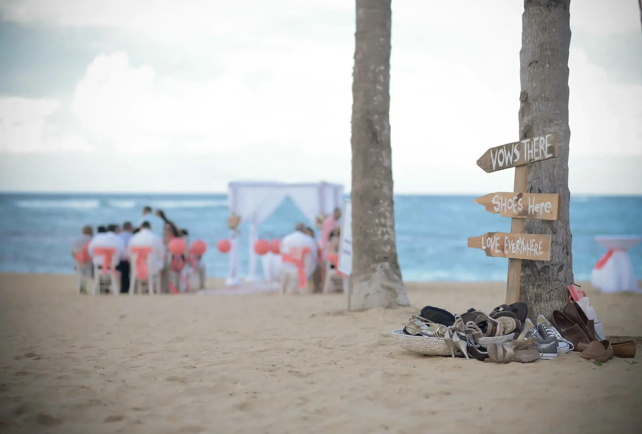 Wooden wedding signs and a pile of guest shoes during a beach ceremony at Dreams Onyx, Punta Cana