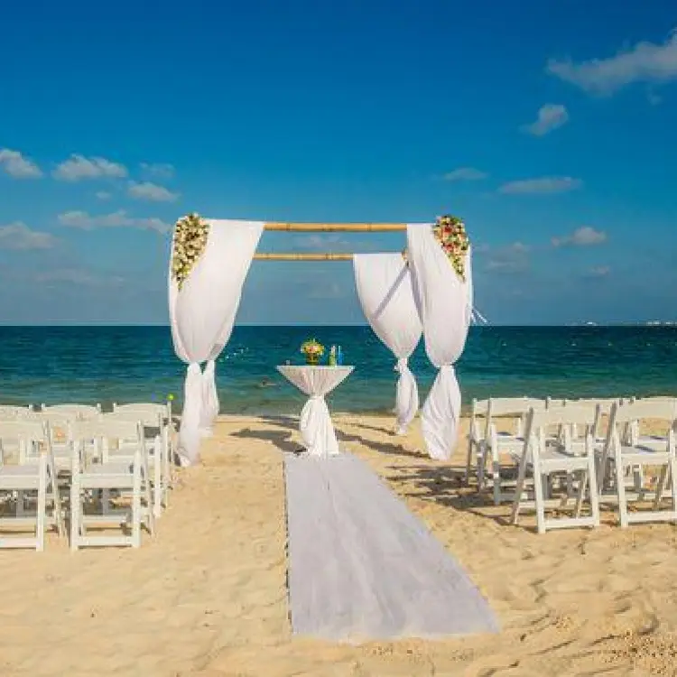 Beachfront wedding ceremony with a white fabric arch and folding chairs at Dreams Playa Mujeres, Cancun