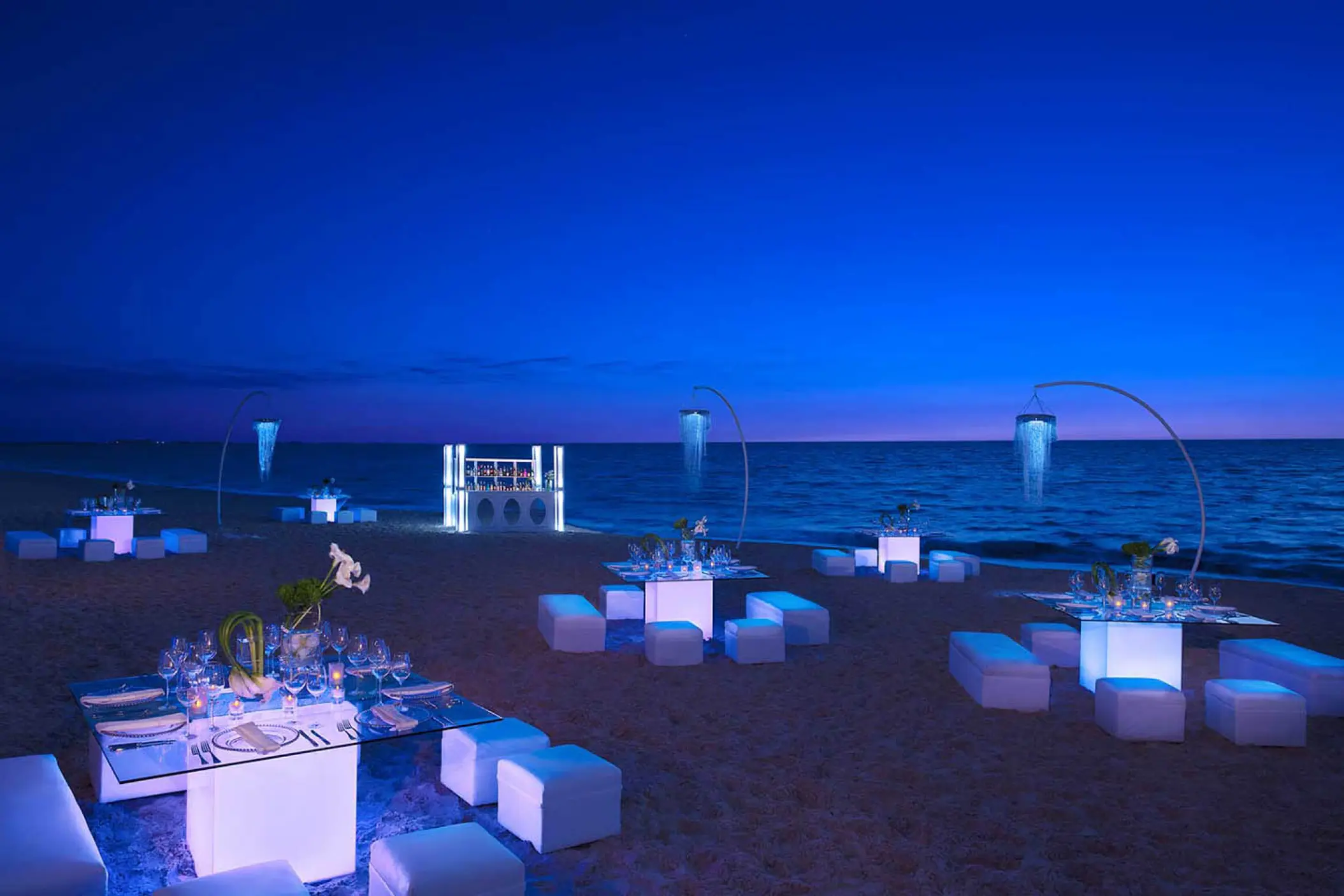 Beachfront wedding reception with illuminated tables and bar at night at Dreams Playa Mujeres, Cancun