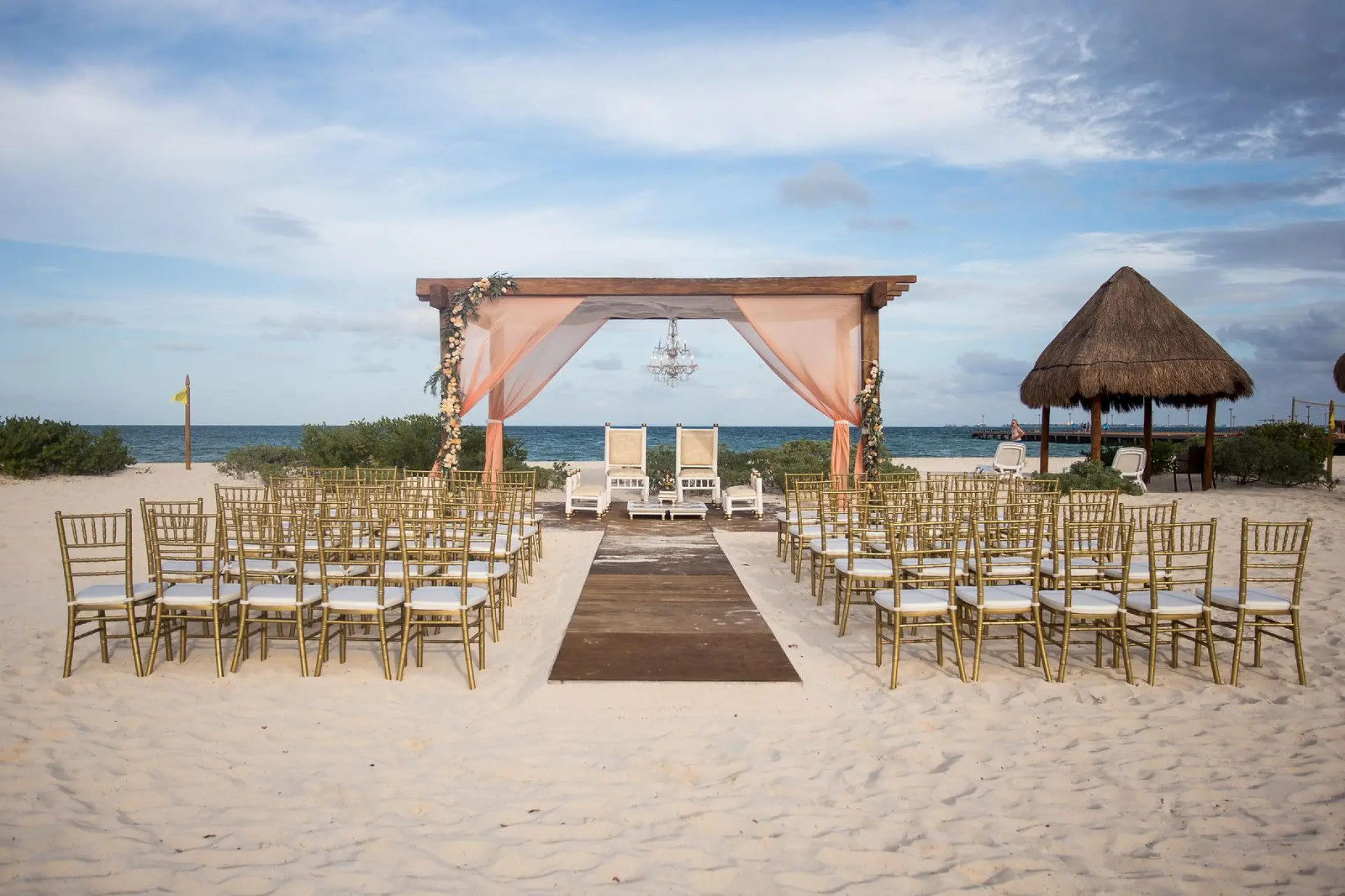 Beach wedding ceremony with a wooden pergola and gold chairs at Dreams Playa Mujeres, Cancun