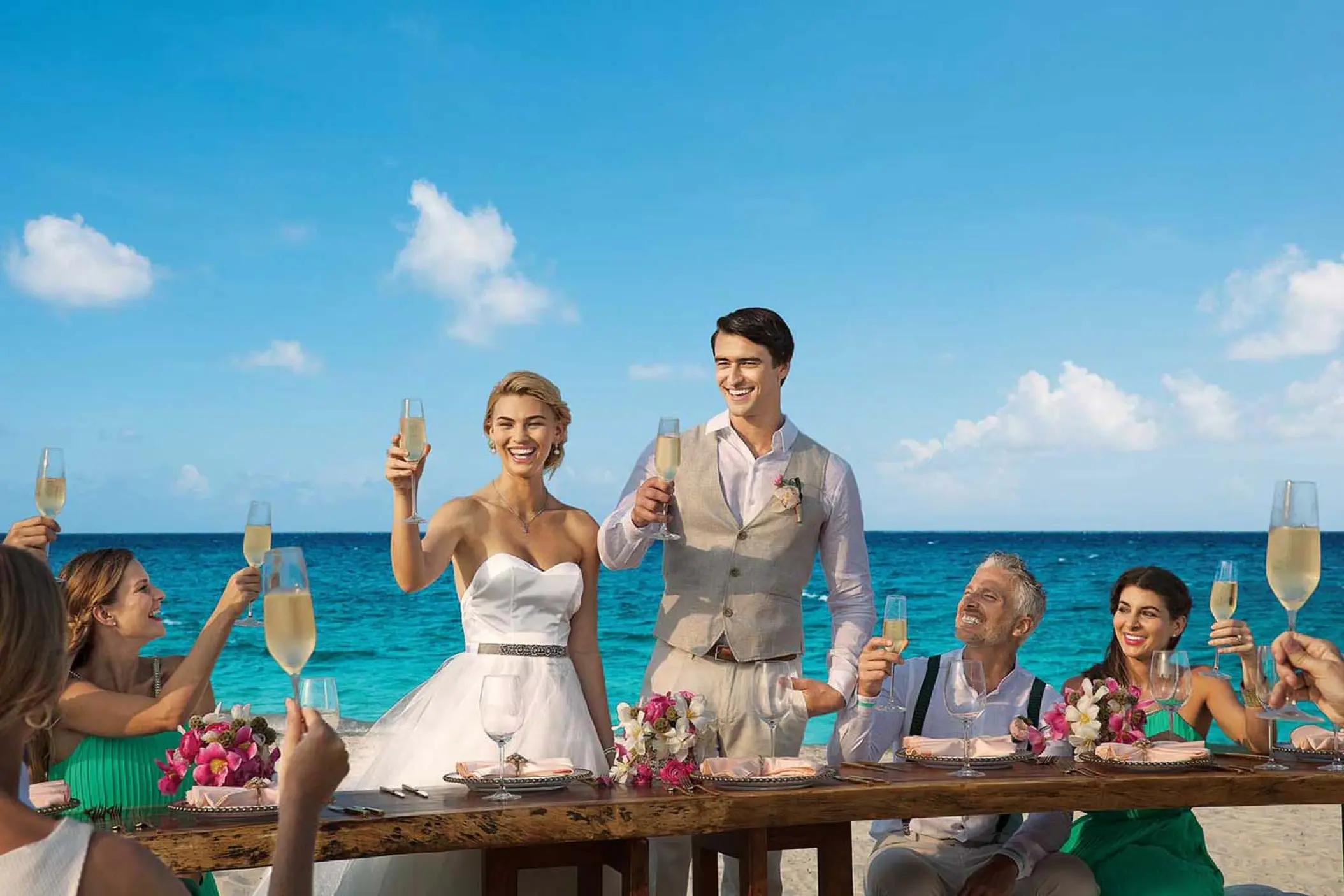 Bride and groom raising a champagne toast at a beach wedding reception at Dreams Playa Mujeres, Cancun