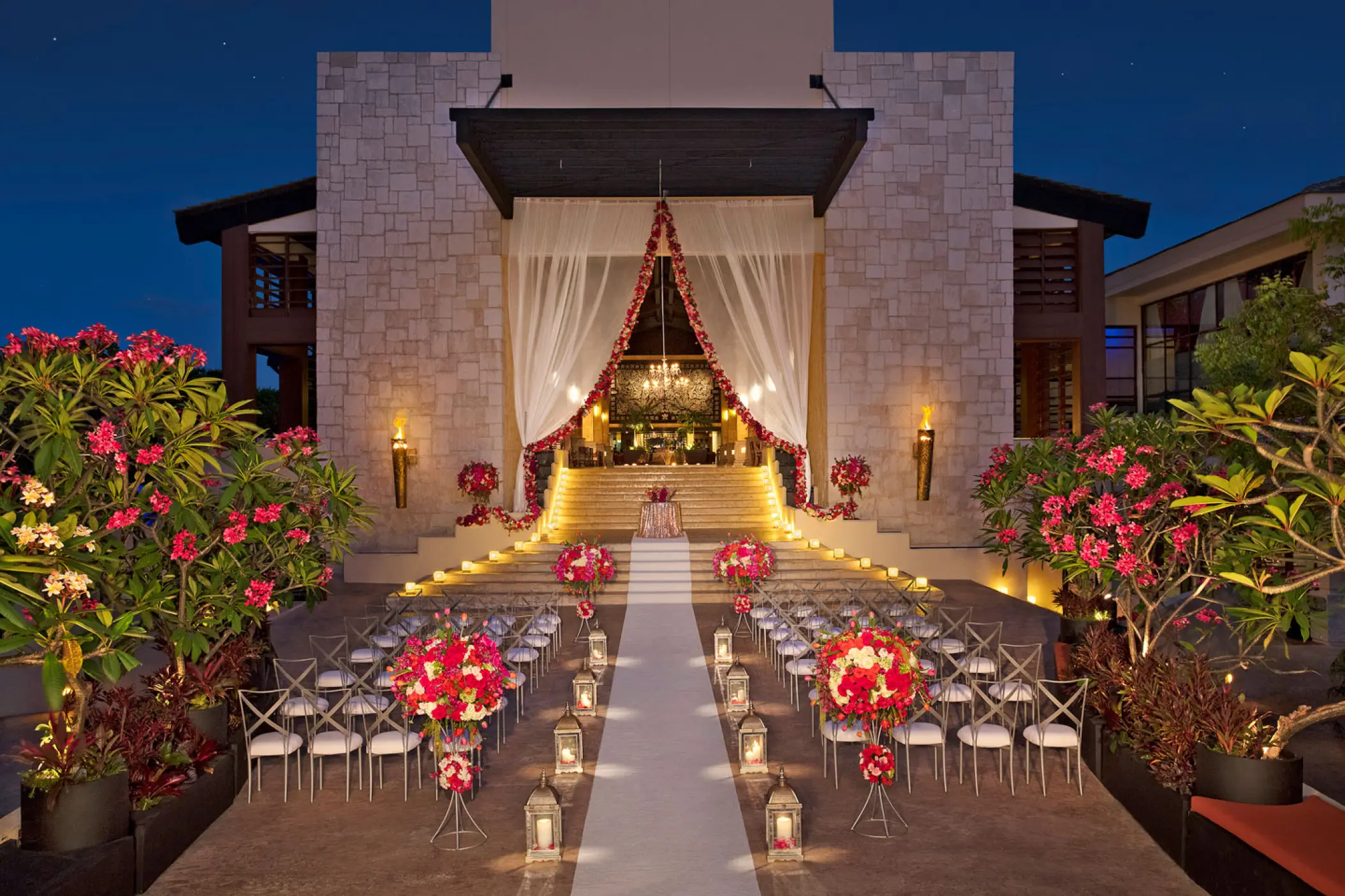 Evening wedding ceremony setup with white aisle and pink floral arrangements at Dreams Riviera Cancun, Riviera Maya