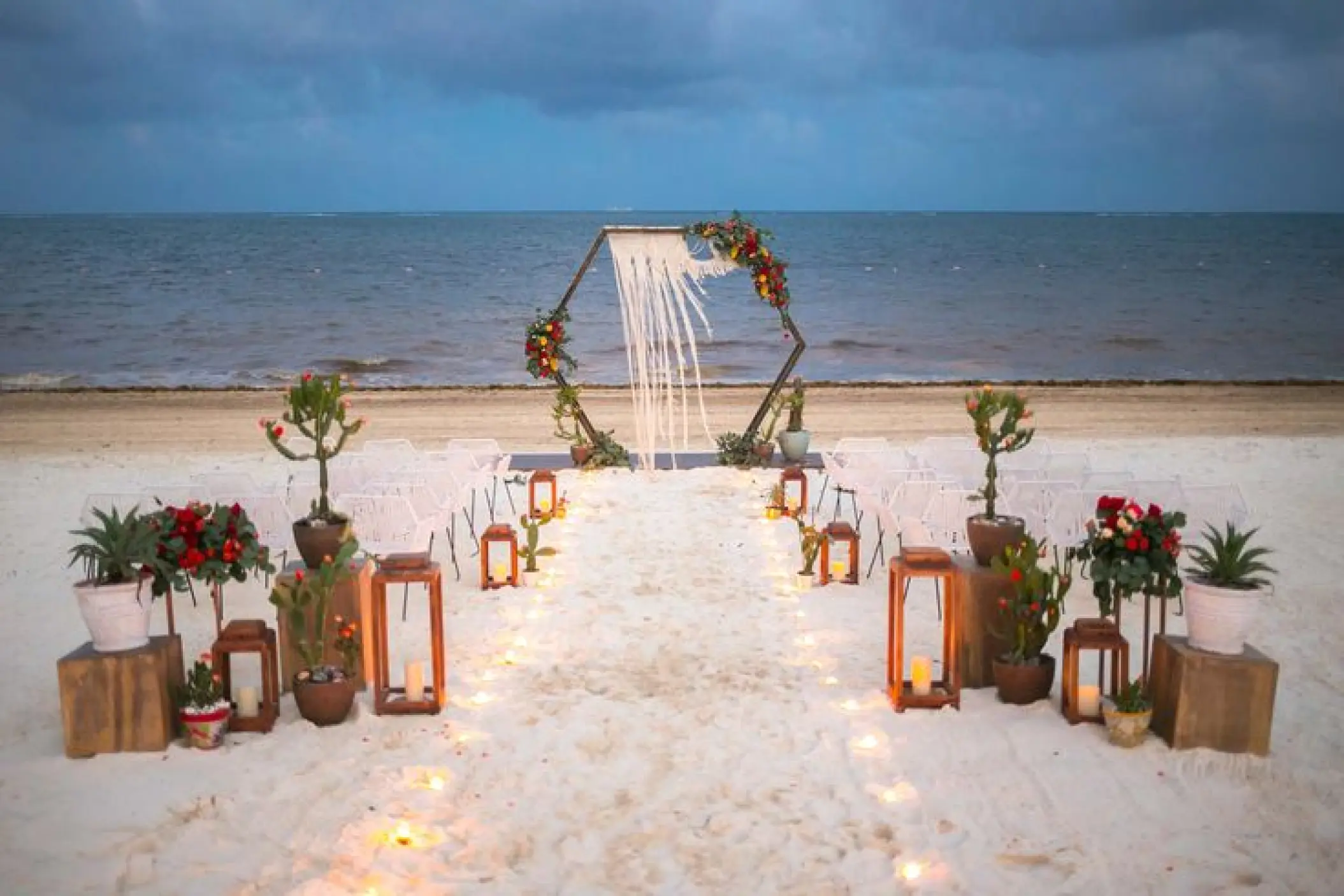Beachfront wedding ceremony setup with lantern aisle and hexagonal arch at Dreams Riviera Cancun, Riviera Maya