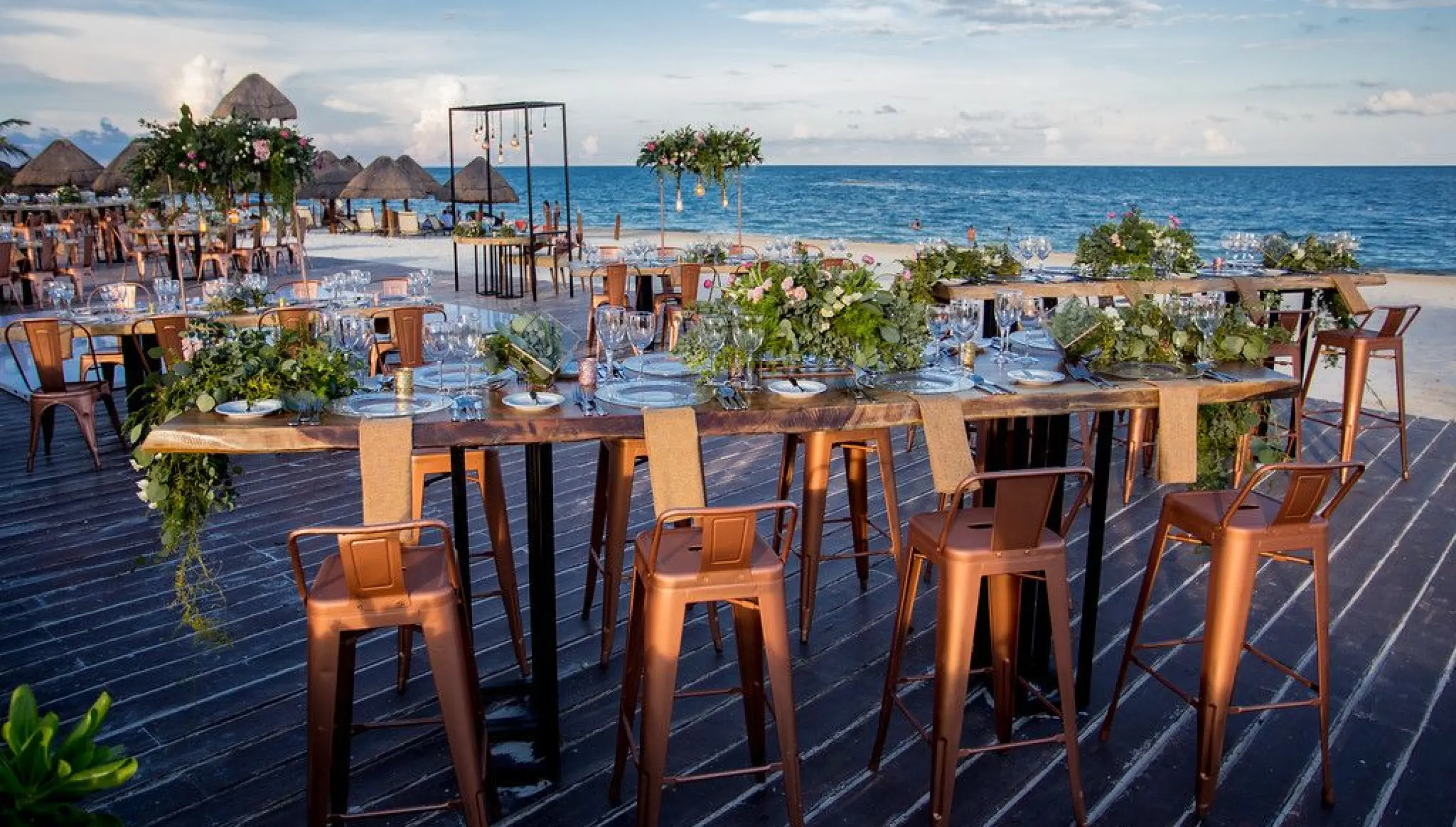 Outdoor wedding reception with long wooden tables and copper stools on the deck at Dreams Riviera Cancun, Riviera Maya