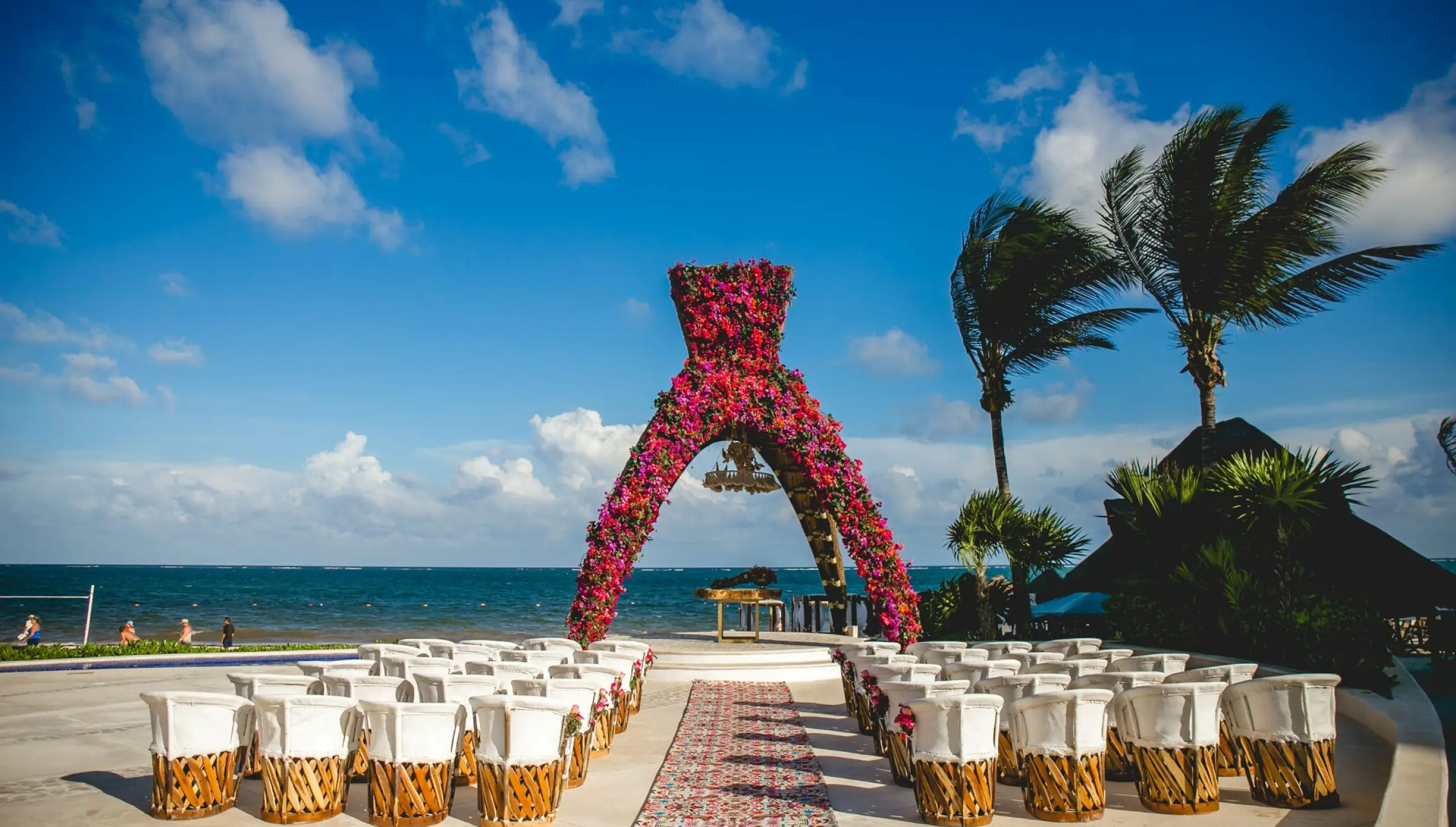 Beachfront wedding ceremony with a pink floral arch and white chairs at Dreams Riviera Cancun, Riviera Maya