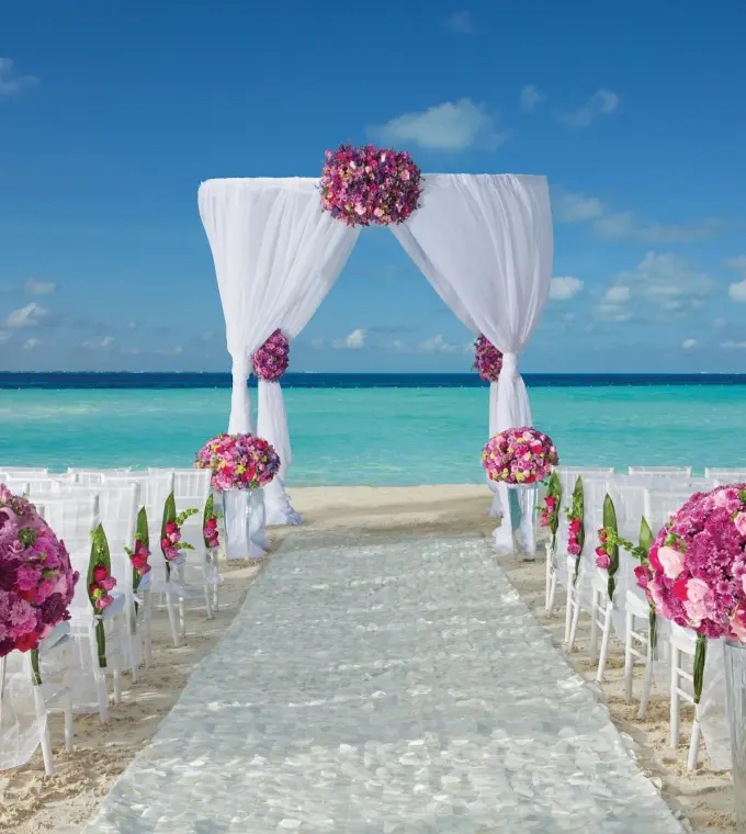 Beach wedding ceremony with pink floral arrangements and white arch at Dreams Sands Cancun, Cancun