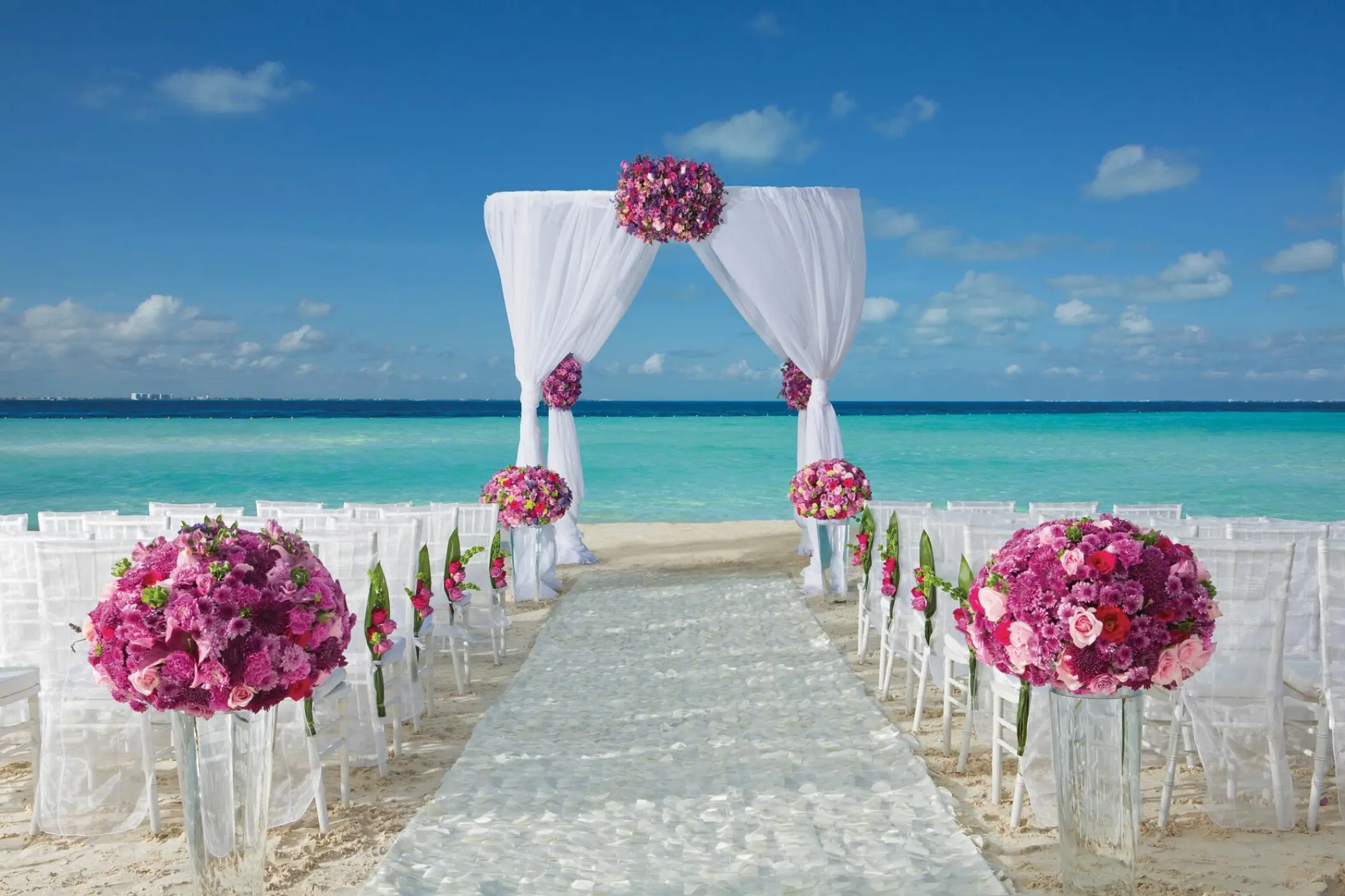 Beach wedding ceremony with pink floral arrangements and white arch at Dreams Sands Cancun, Cancun