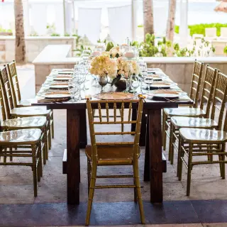 Long wooden wedding reception table with gold chairs at Dreams Sands Cancun