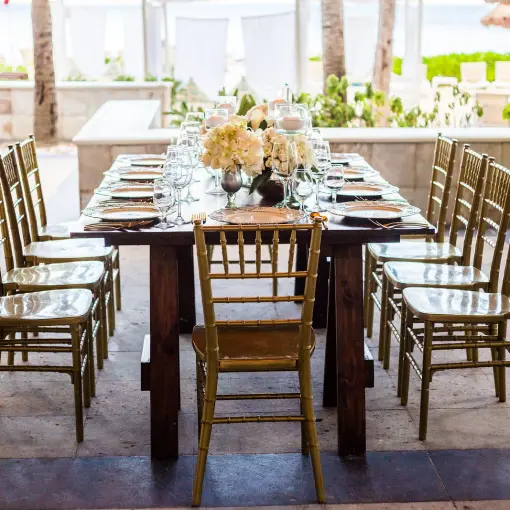 Long wooden wedding reception table with gold chairs at Dreams Sands Cancun
