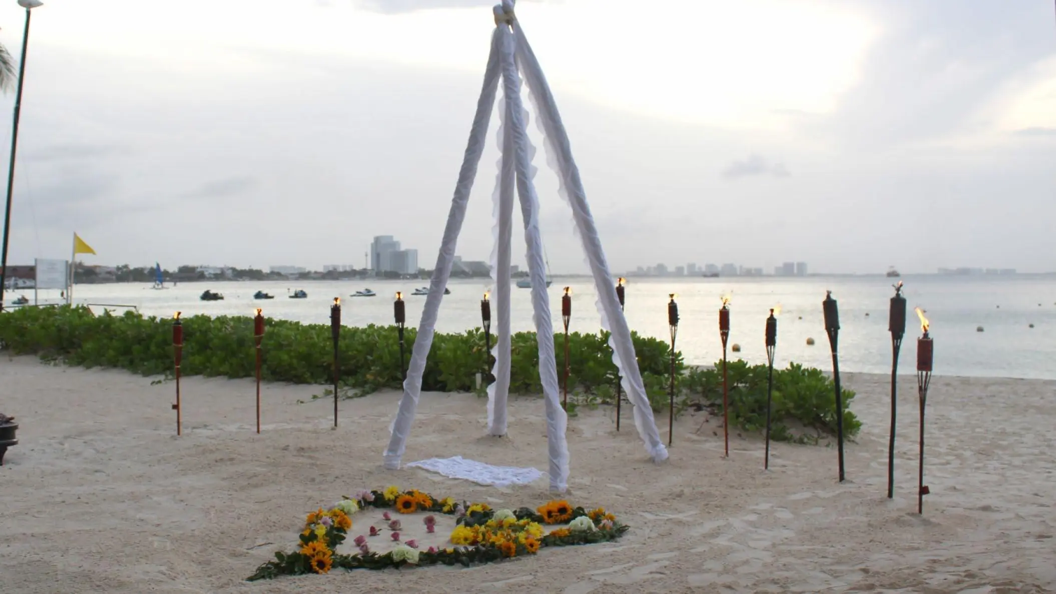Teepee wedding ceremony setup with tiki torches and sunflower heart on the beach at Dreams Sands Cancun, Cancun