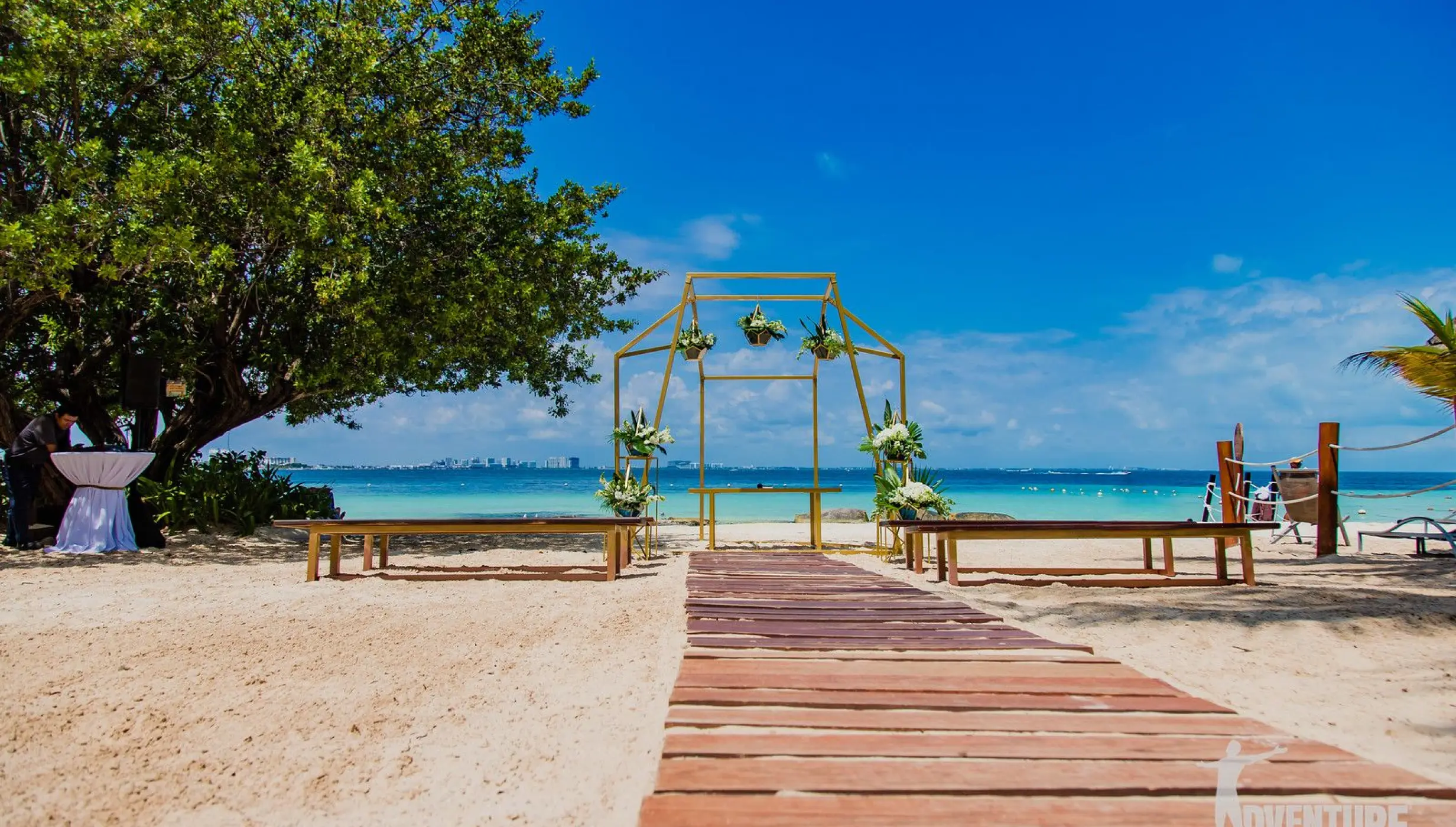 Beachfront wedding ceremony with a gold arch and wooden aisle at Dreams Sands, Cancun