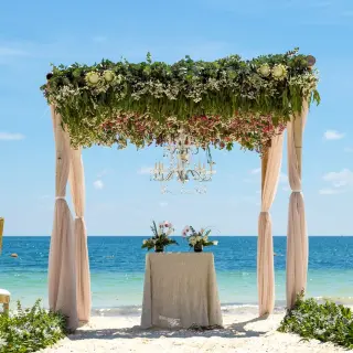 Beachfront wedding ceremony with a floral huppah and chandelier at Dreams Sapphire, Riviera Maya