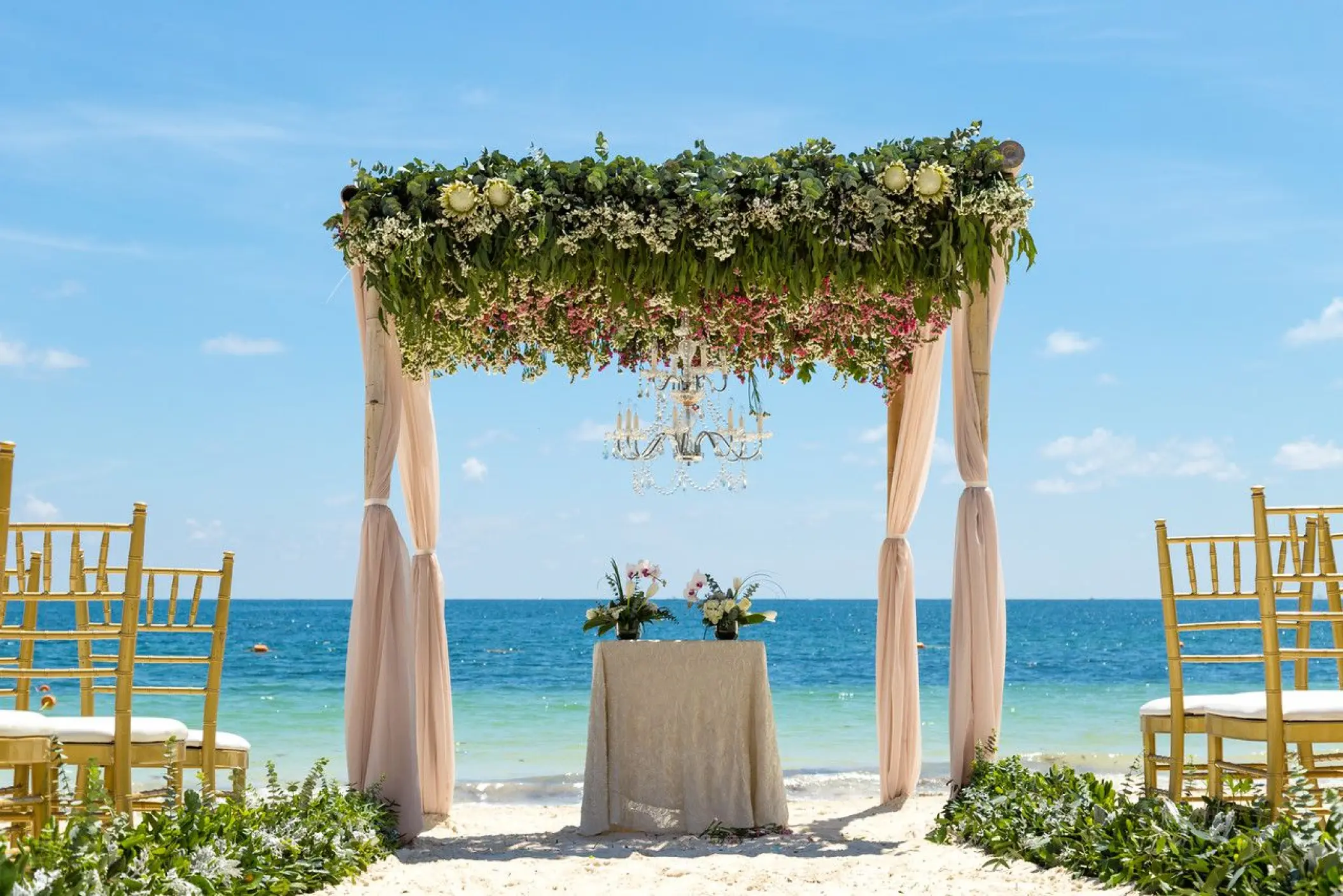 Beachfront wedding ceremony with a floral huppah and chandelier at Dreams Sapphire, Riviera Maya
