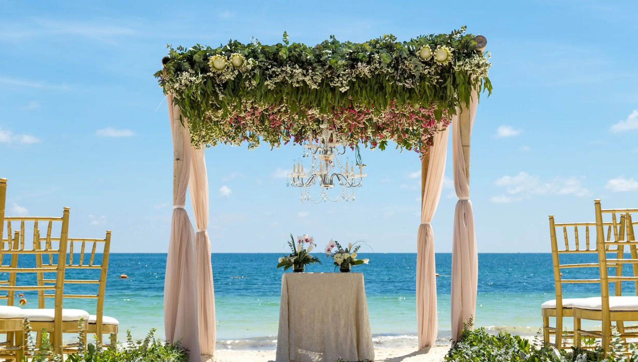 Beachfront wedding ceremony with a floral huppah and chandelier at Dreams Sapphire, Riviera Maya