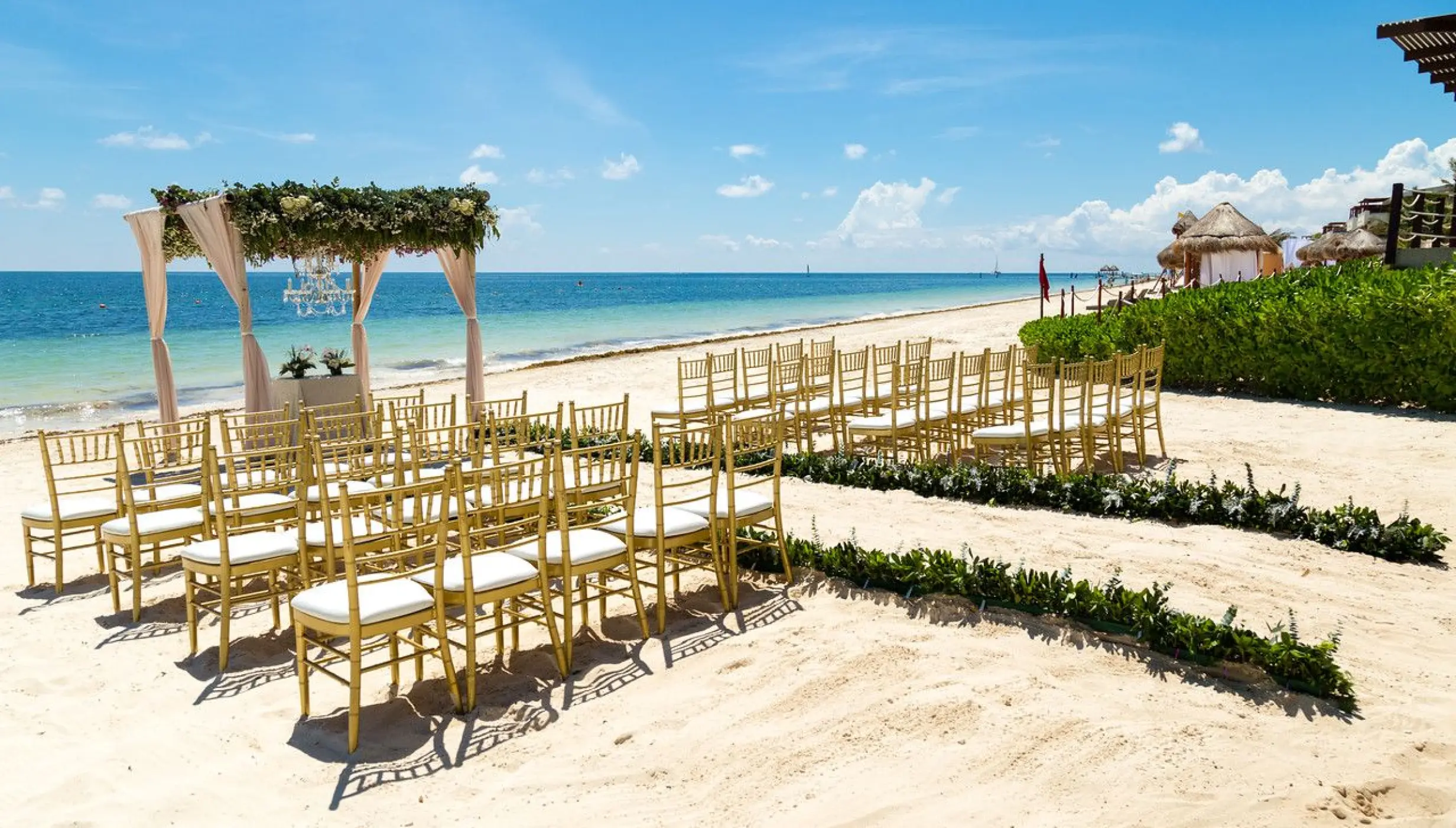 Beachfront wedding ceremony with gold chairs and floral arch at Dreams Sapphire, Riviera Maya