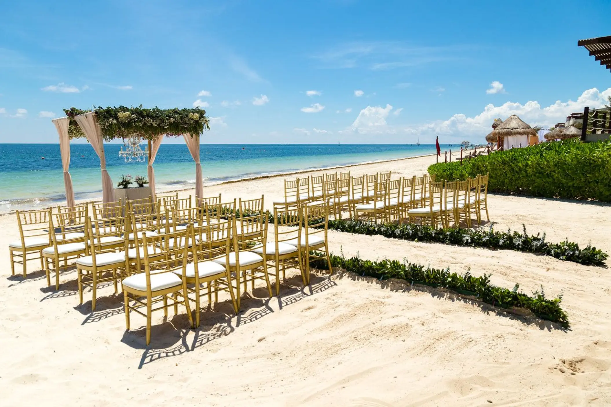 Beachfront wedding ceremony with gold chairs and floral arch at Dreams Sapphire, Riviera Maya