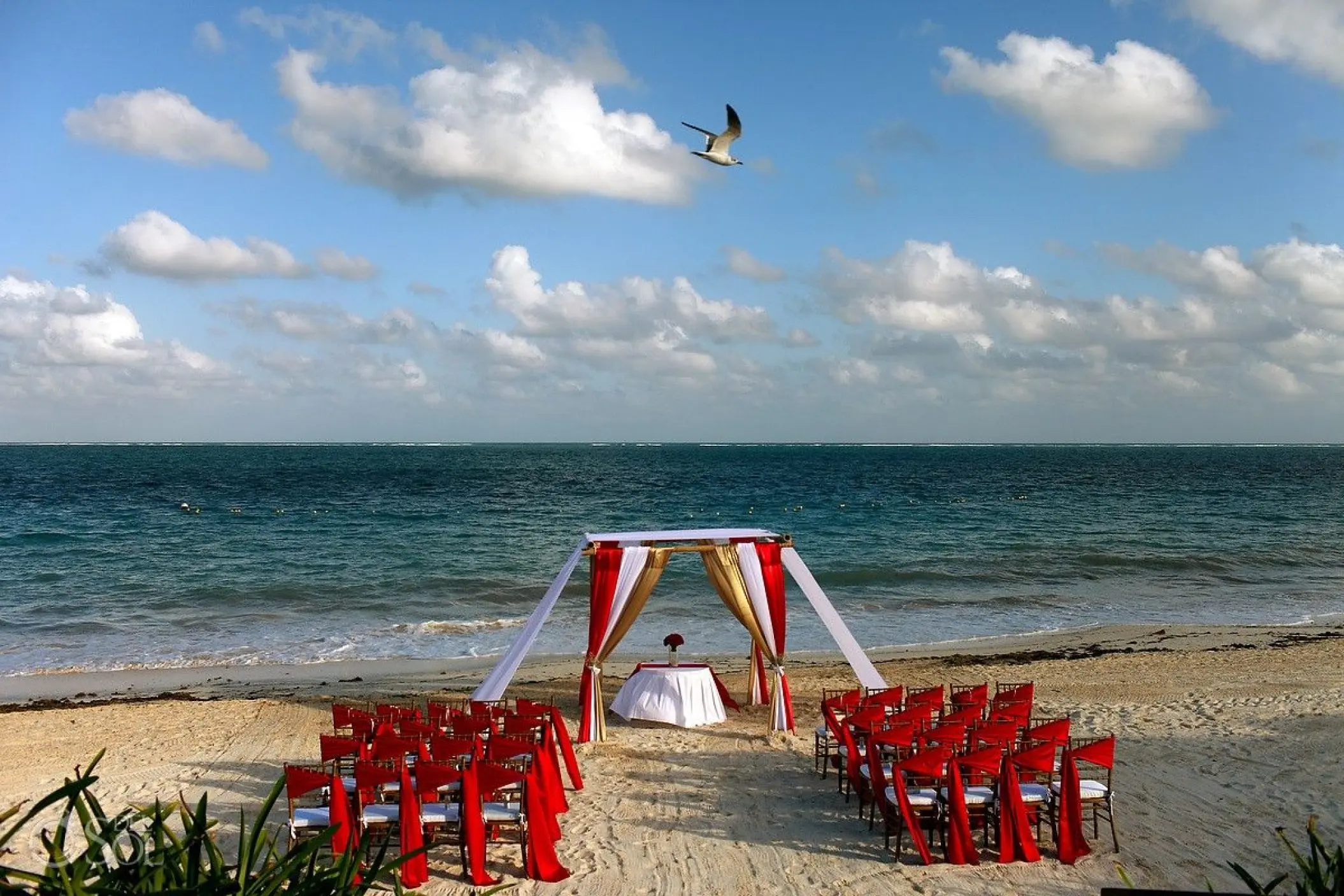 Beachfront wedding ceremony with red chairs and fabric huppah at Dreams Sapphire, Riviera Maya