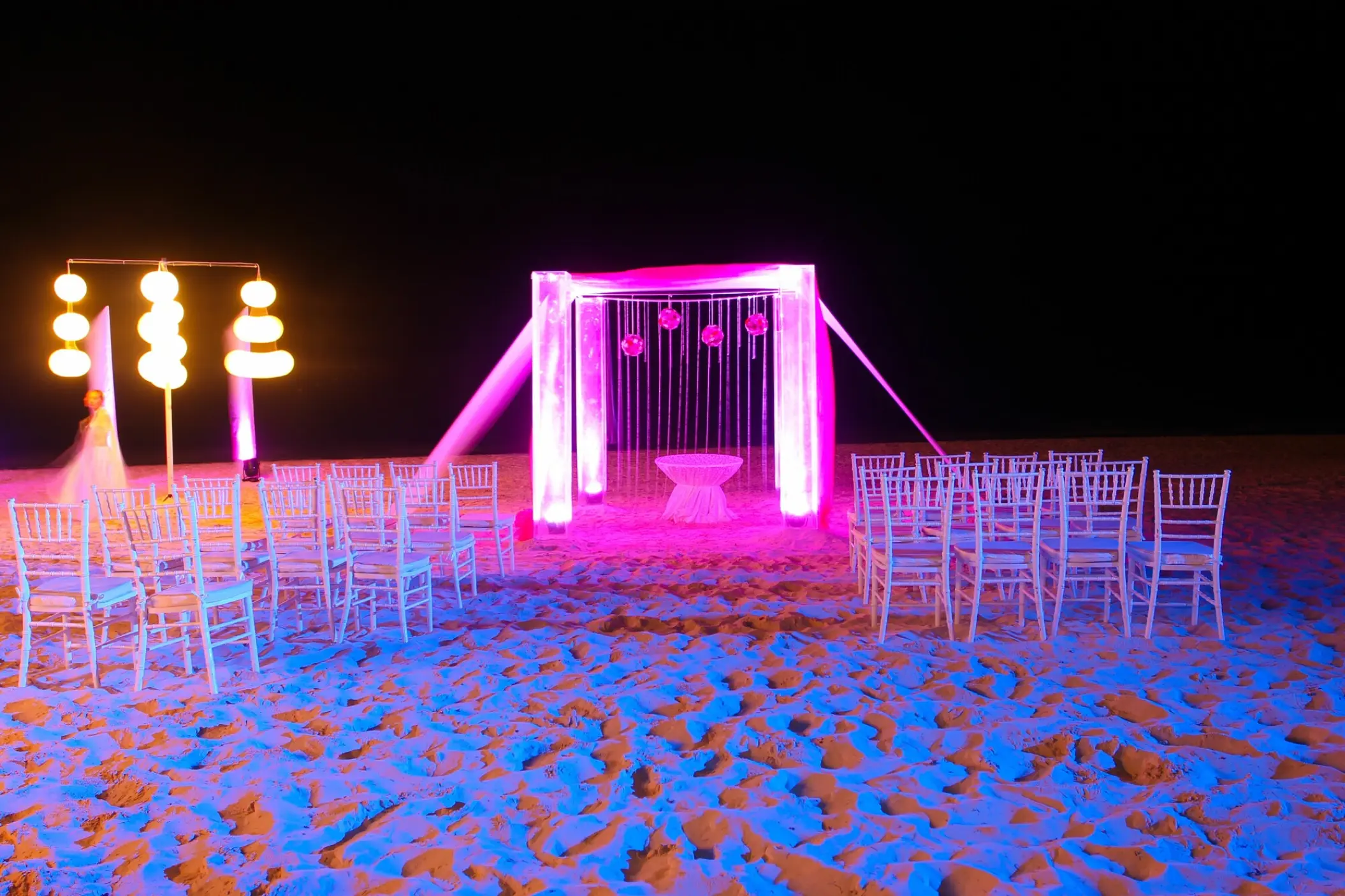 Beach wedding ceremony setup at night with pink lighting and white chairs at Dreams Sapphire, Riviera Maya
