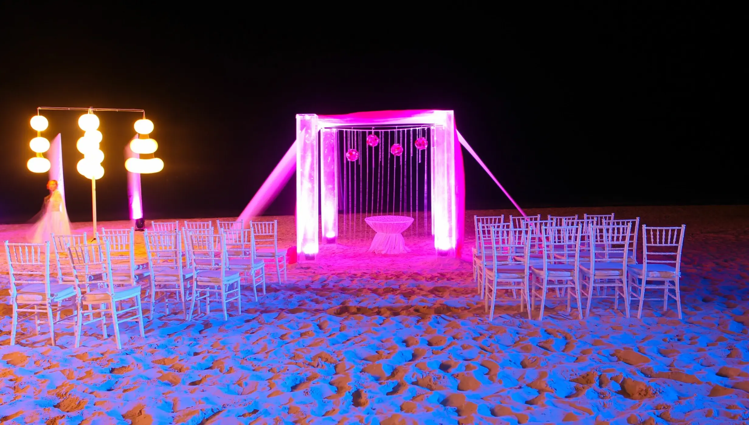 Beach wedding ceremony setup at night with pink lighting and white chairs at Dreams Sapphire, Riviera Maya