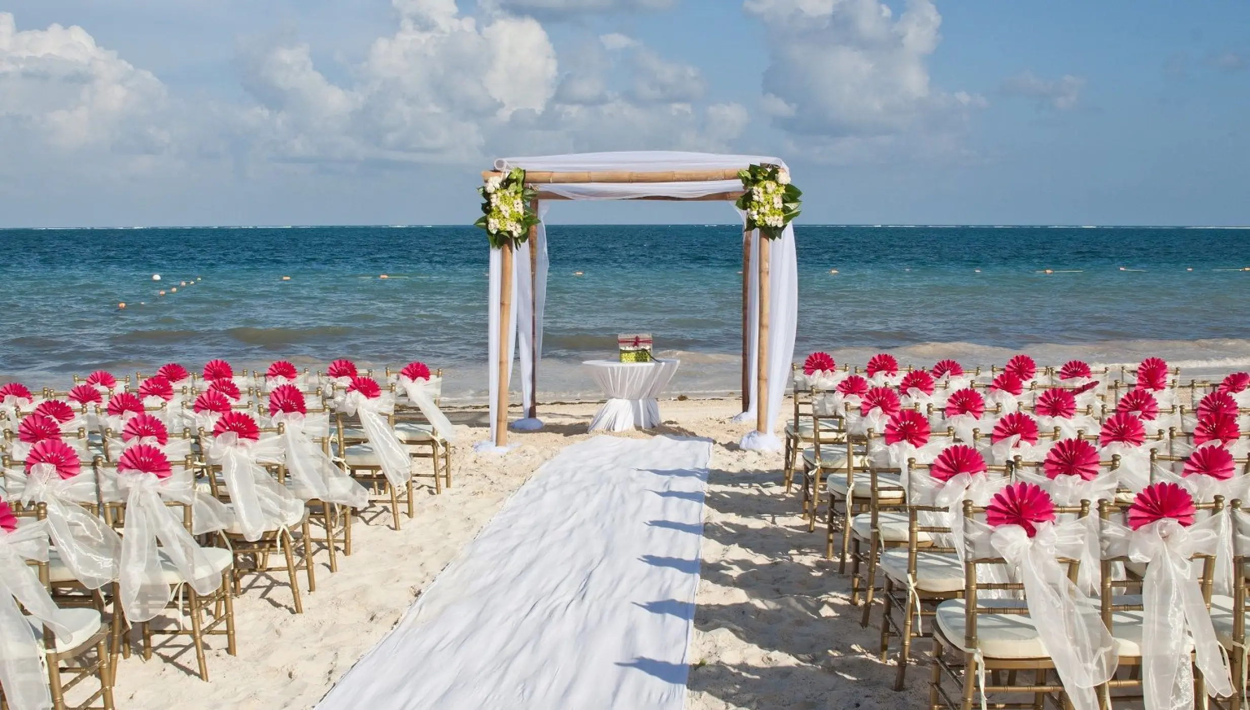 Beach wedding ceremony at Dreams Sapphire, Riviera Maya featuring pink floral chair decor and a wooden arch