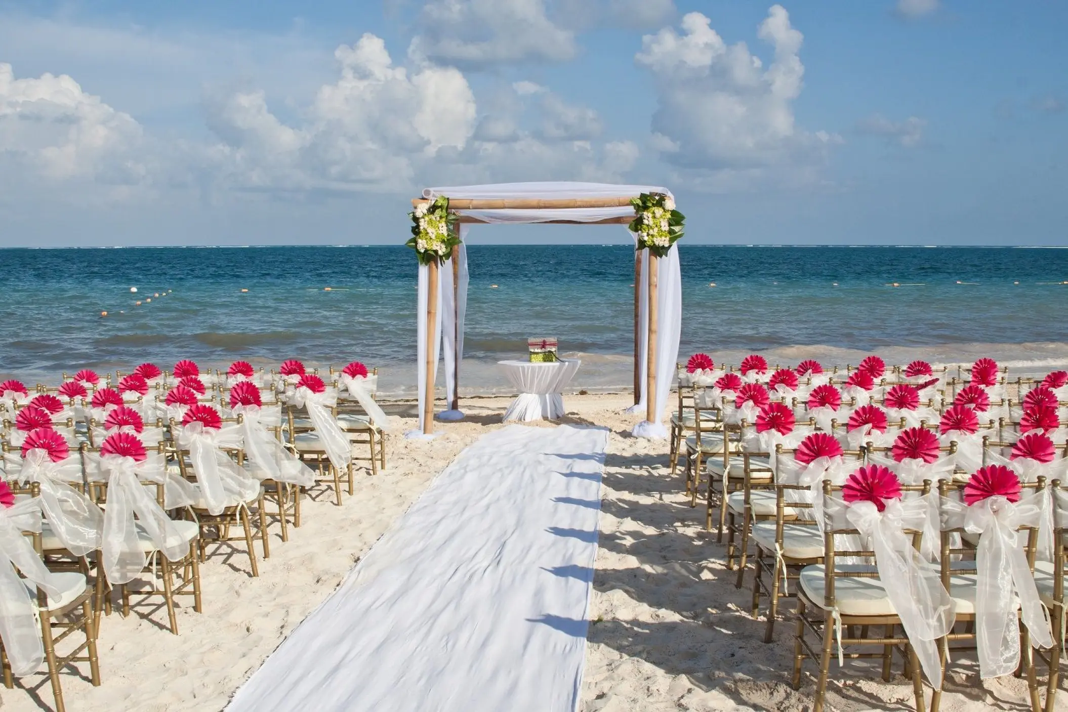 Beach wedding ceremony at Dreams Sapphire, Riviera Maya featuring pink floral chair decor and a wooden arch
