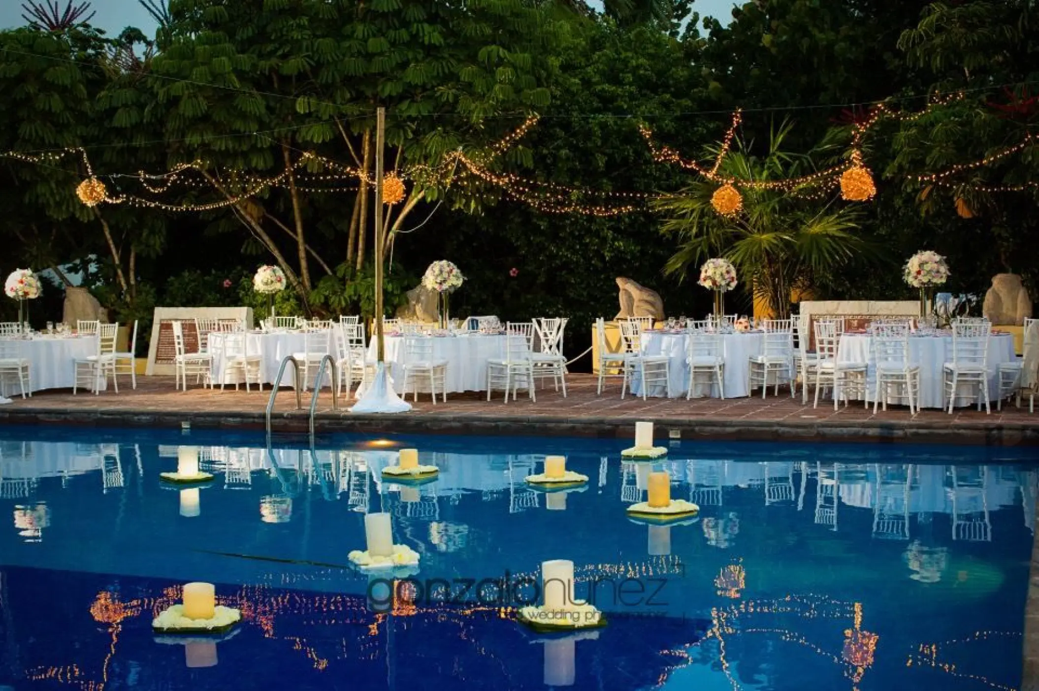 Poolside wedding reception with floating candles and string lights at Dreams Sapphire, Riviera Maya