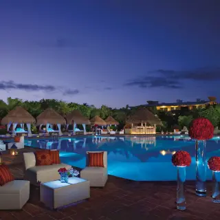 Nighttime pool party setup with glowing tables and red floral decor at Dreams Sapphire, Riviera Maya
