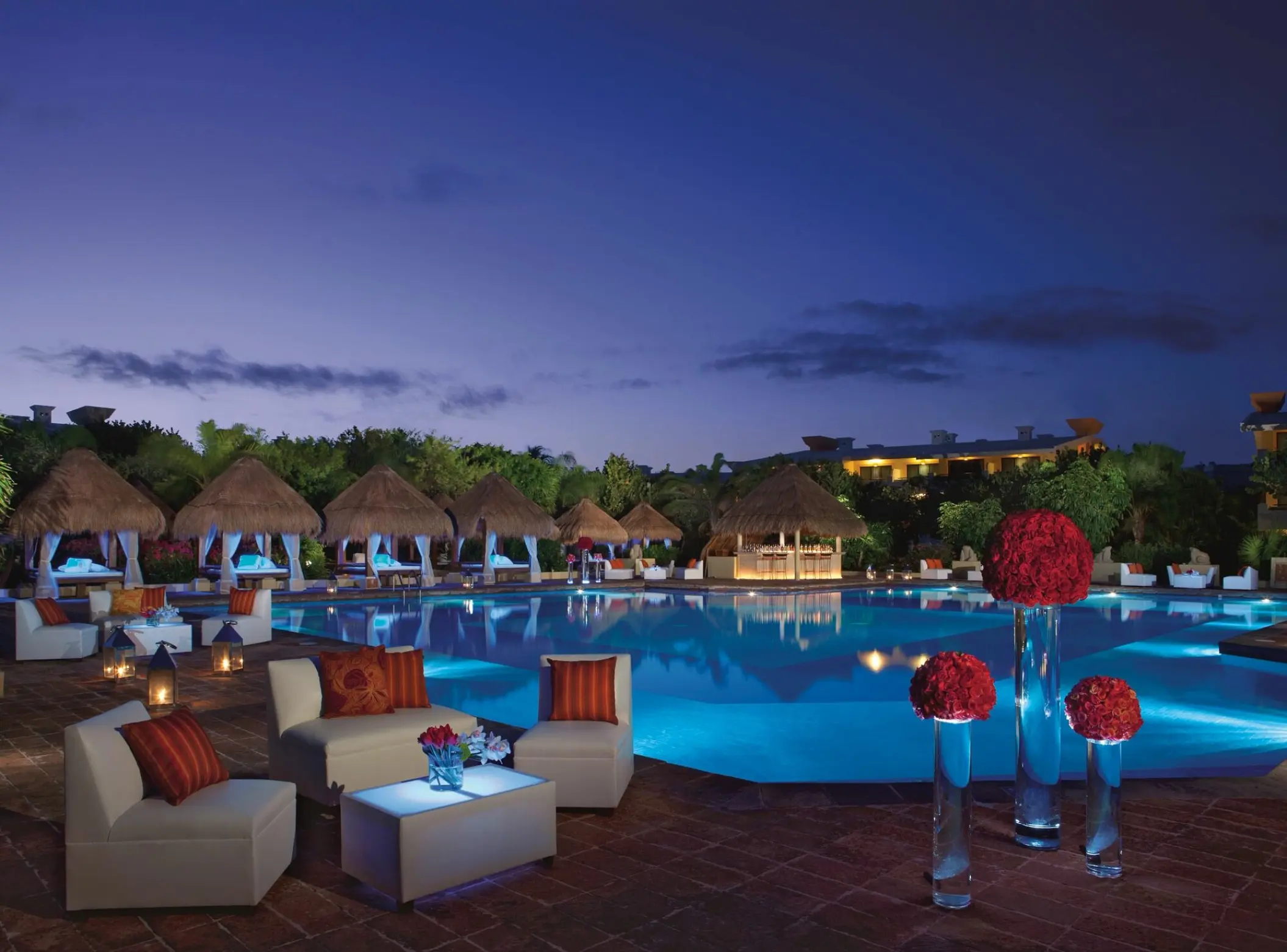 Nighttime pool party setup with glowing tables and red floral decor at Dreams Sapphire, Riviera Maya