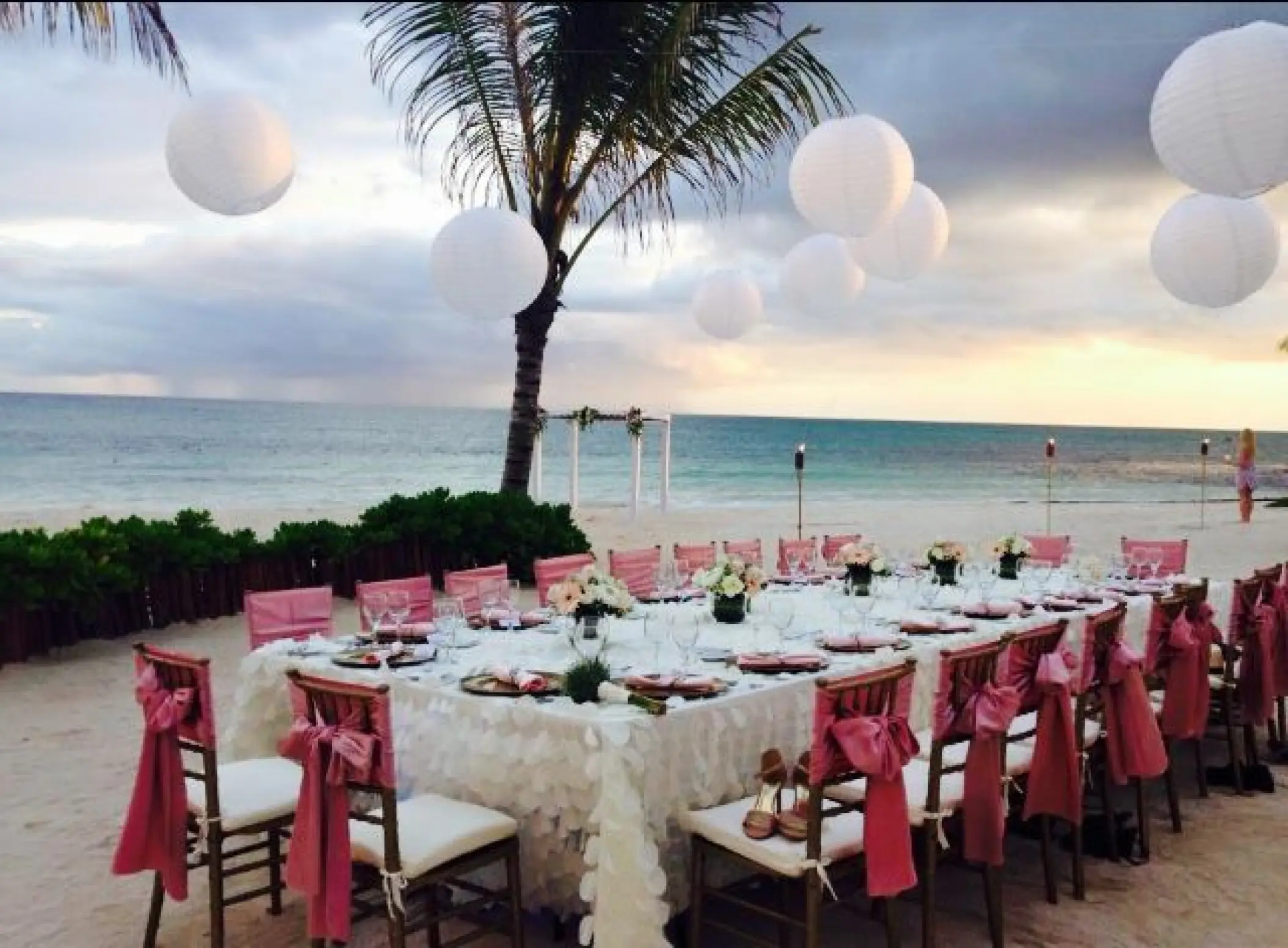 Beachfront wedding reception with pink chair bows and white lanterns at Dreams Tulum, Tulum