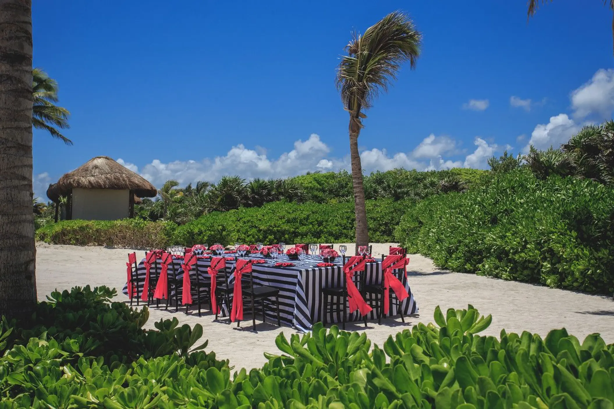 Beachfront wedding reception table with striped linens and red sashes at Dreams Tulum, Tulum