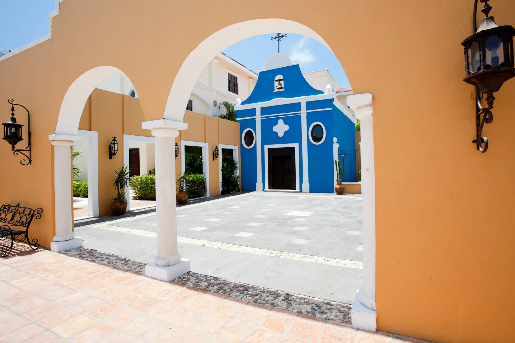 Mexican plaza and bright blue chapel seen through stone arches at Dreams Tulum, Tulum