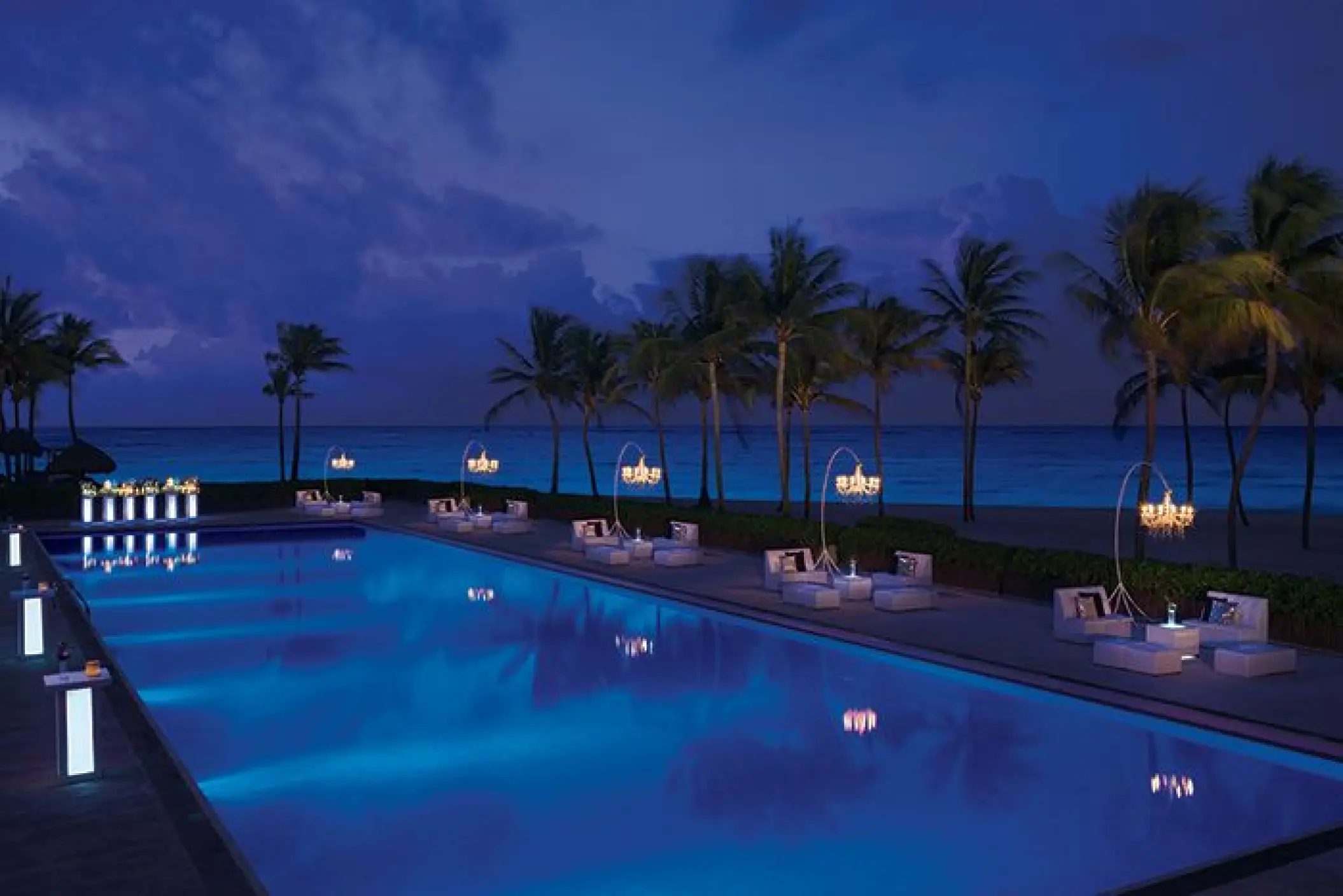 Lit pool terrace at night with chandeliers and lounge seating at Dreams Tulum