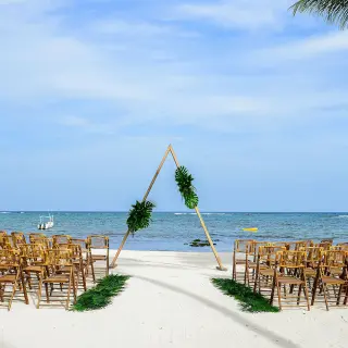 Beachfront wedding ceremony with a triangle arch and wooden chairs at Dreams Tulum, Tulum