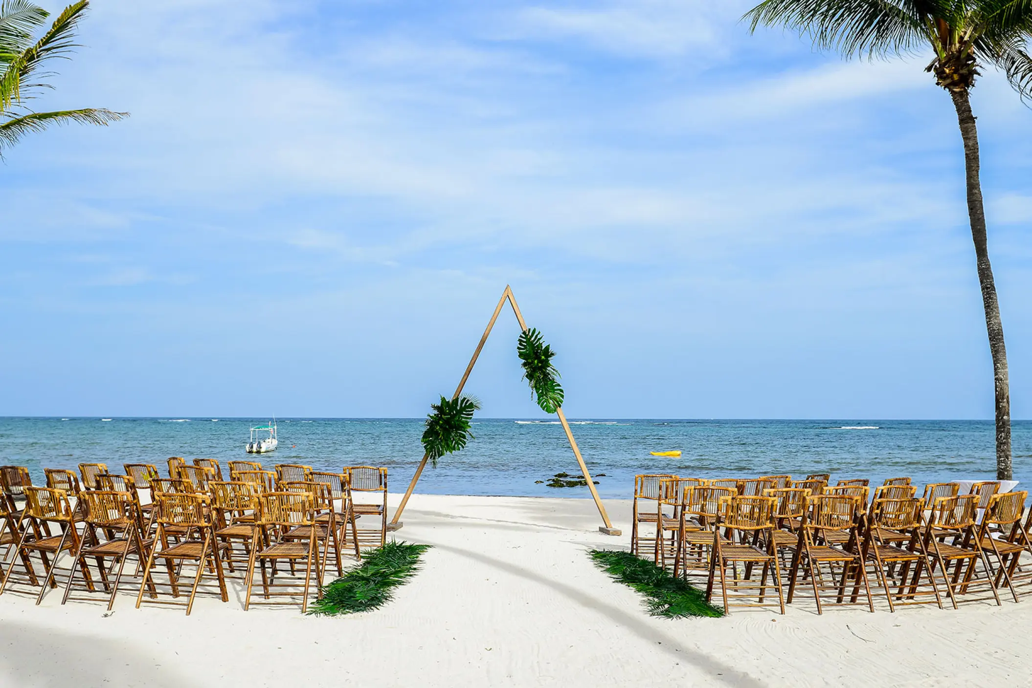 Beachfront wedding ceremony with a triangle arch and wooden chairs at Dreams Tulum, Tulum