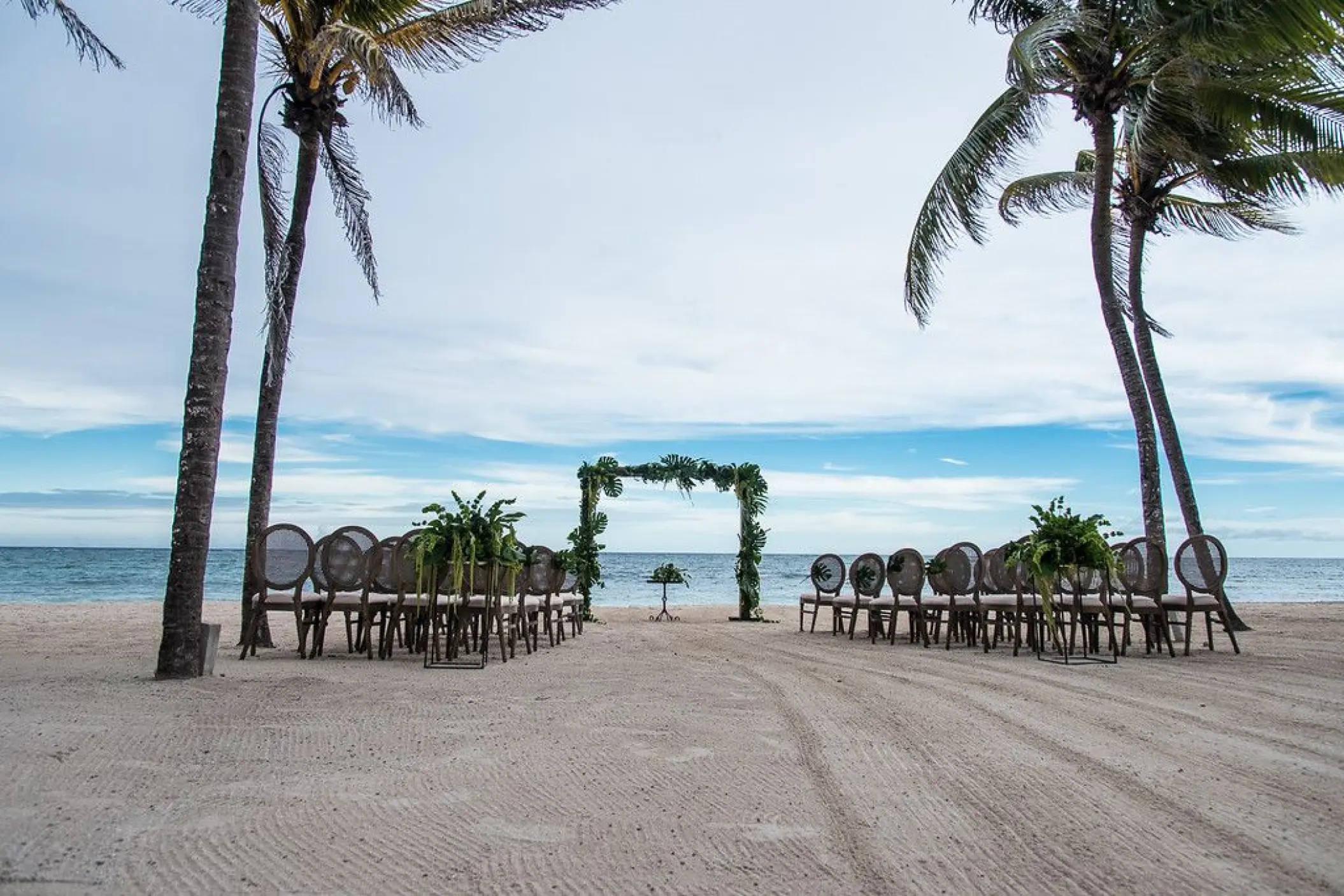 Beachfront wedding ceremony setup with a greenery arch at Dreams Tulum, Tulum
