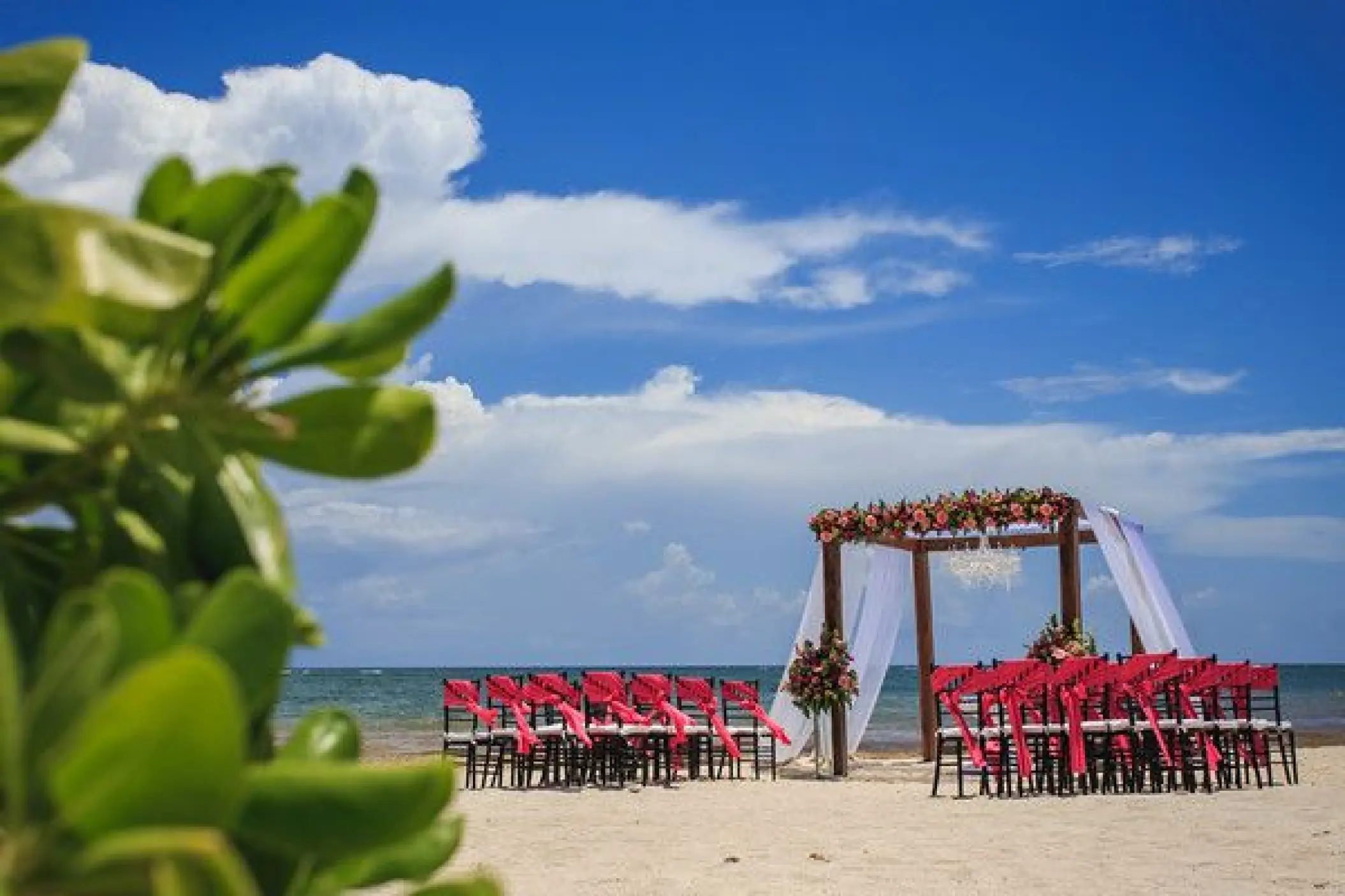 Beachfront wedding ceremony with a floral wooden gazebo and red chairs at Dreams Tulum, Tulum