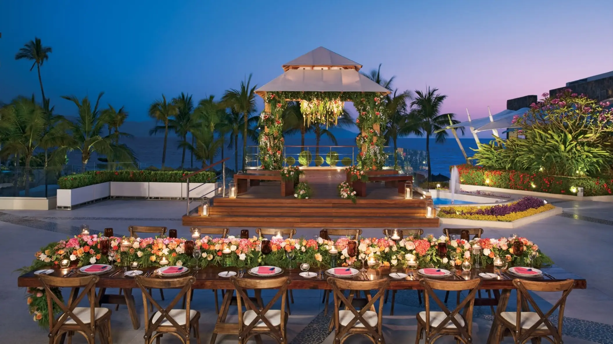 Terrace wedding reception with a floral head table and lit gazebo at Dreams Vallarta Bay, Puerto Vallarta