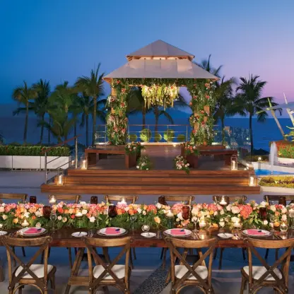 Terrace wedding reception with a floral head table and lit gazebo at Dreams Vallarta Bay, Puerto Vallarta