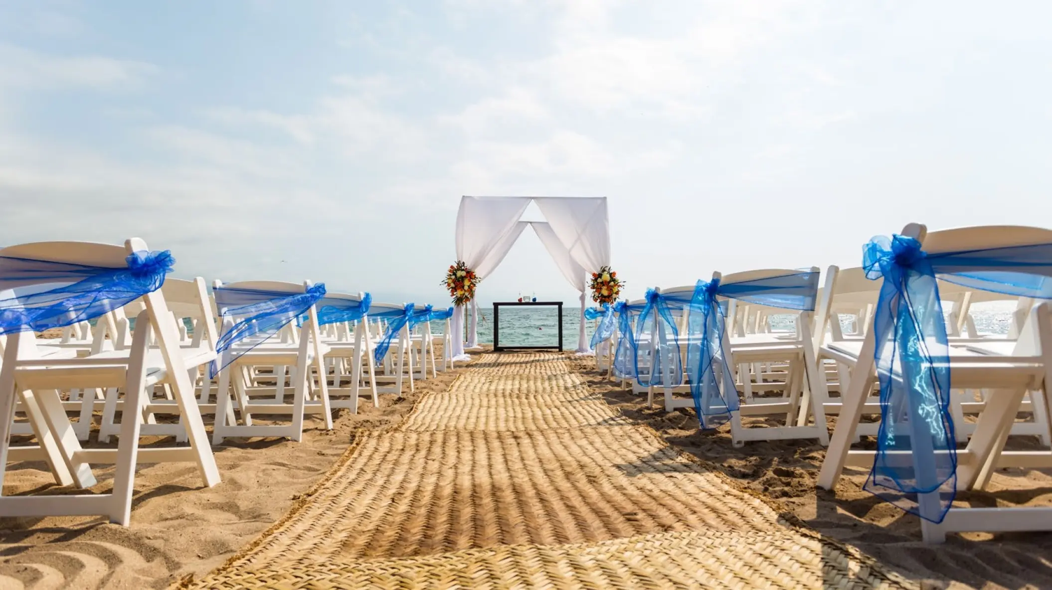 Beachfront wedding ceremony with white chairs and blue sashes at Dreams Vallarta Bay, Puerto Vallarta