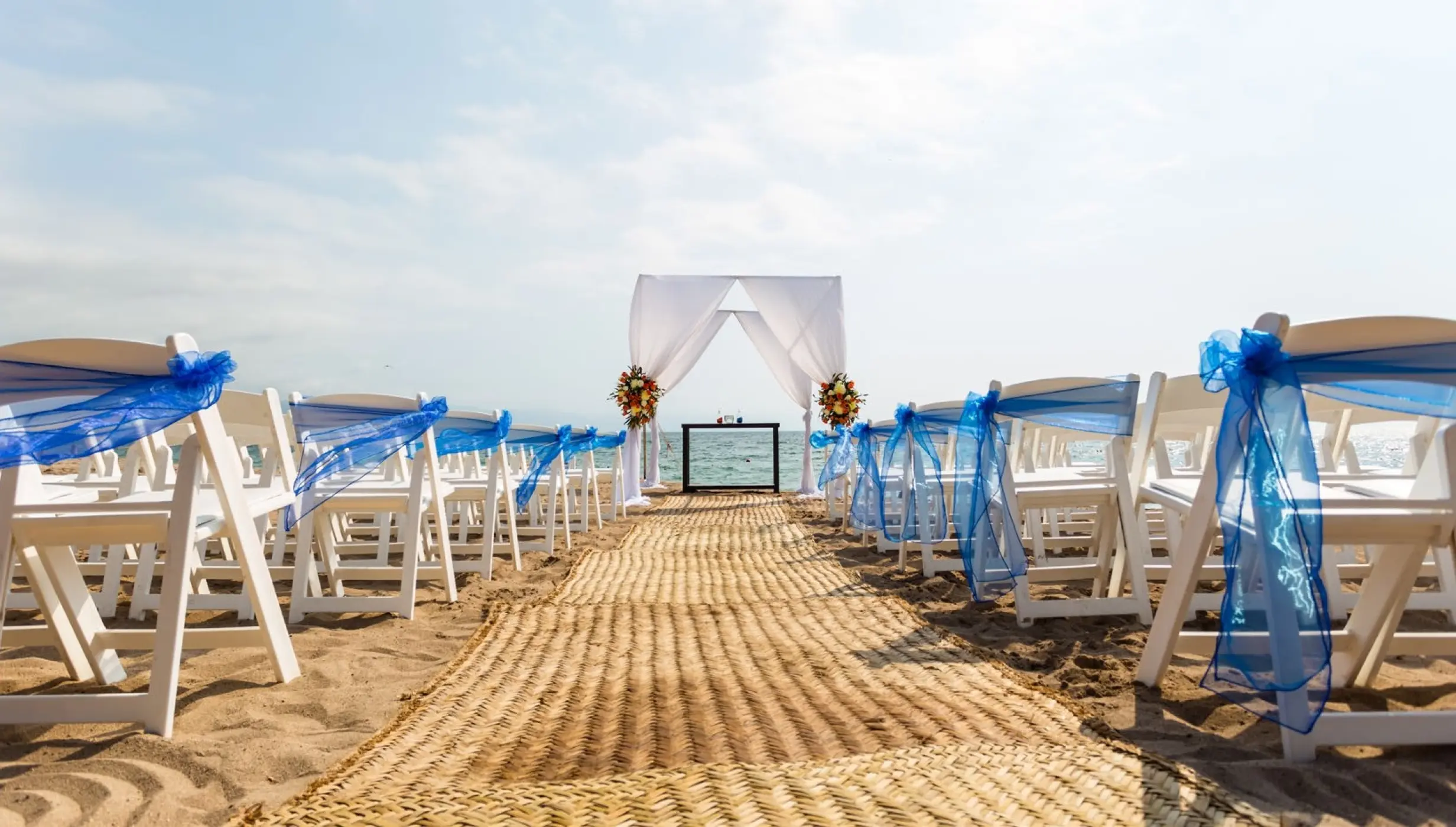Beachfront wedding ceremony with white chairs and blue sashes at Dreams Vallarta Bay, Puerto Vallarta