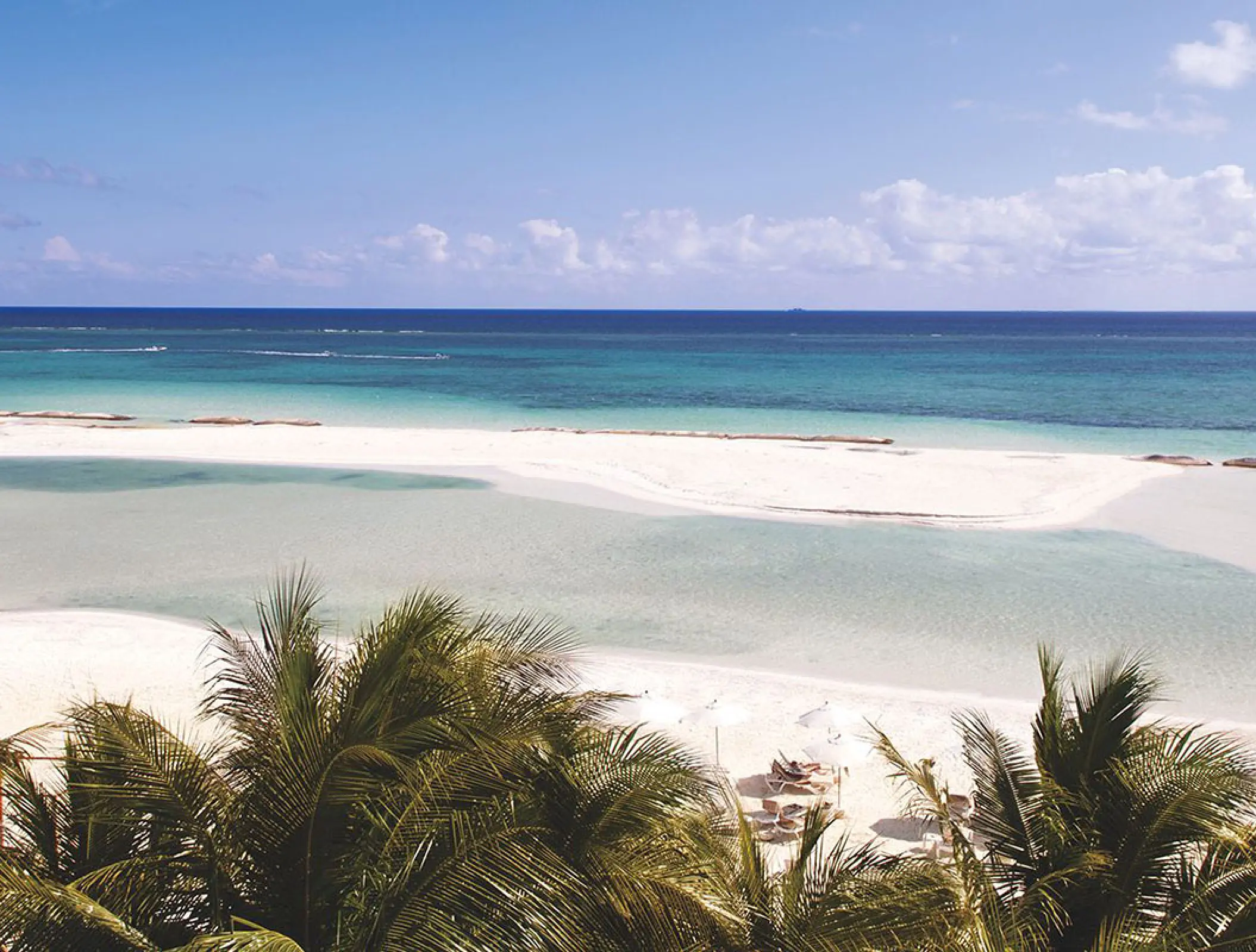 White sand beach and turquoise water behind palm trees at El Dorado Maroma, Riviera Maya