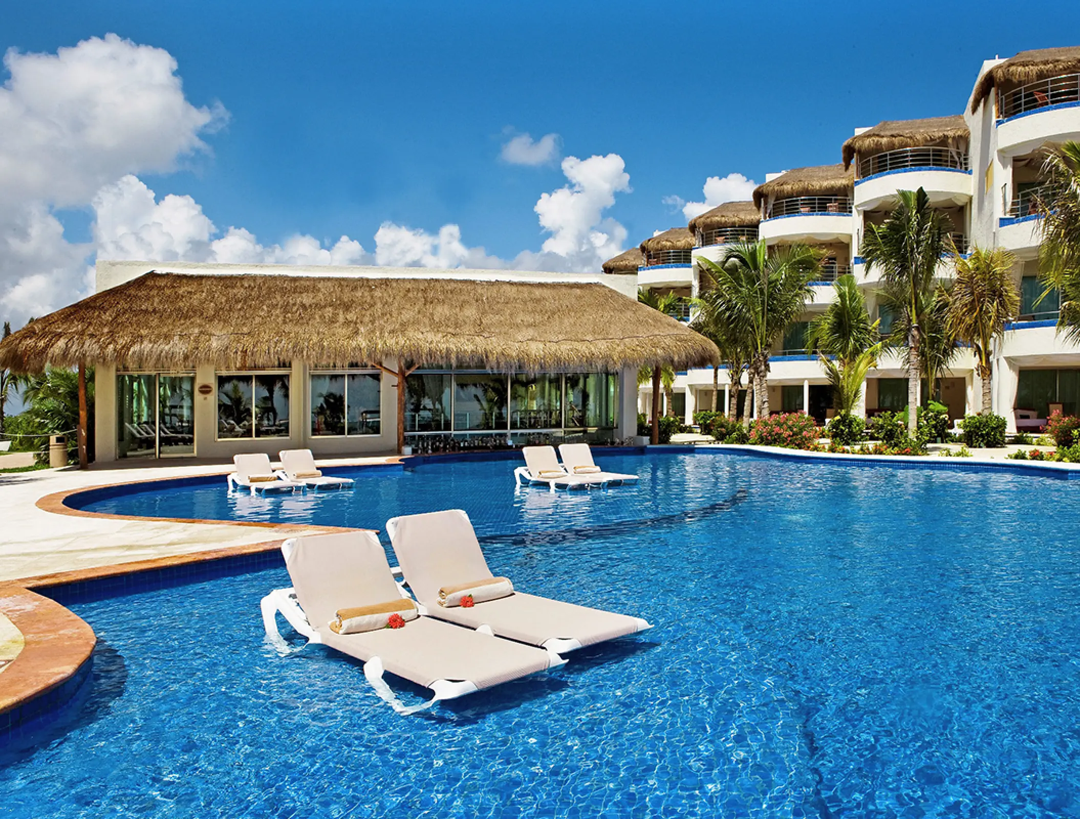 El Dorado Maroma swimming pool with in-water lounge chairs and thatched roof building, Riviera Maya