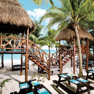 Thatched-roof beach cabins and dining tables at El Dorado Seaside Suites, Riviera Maya